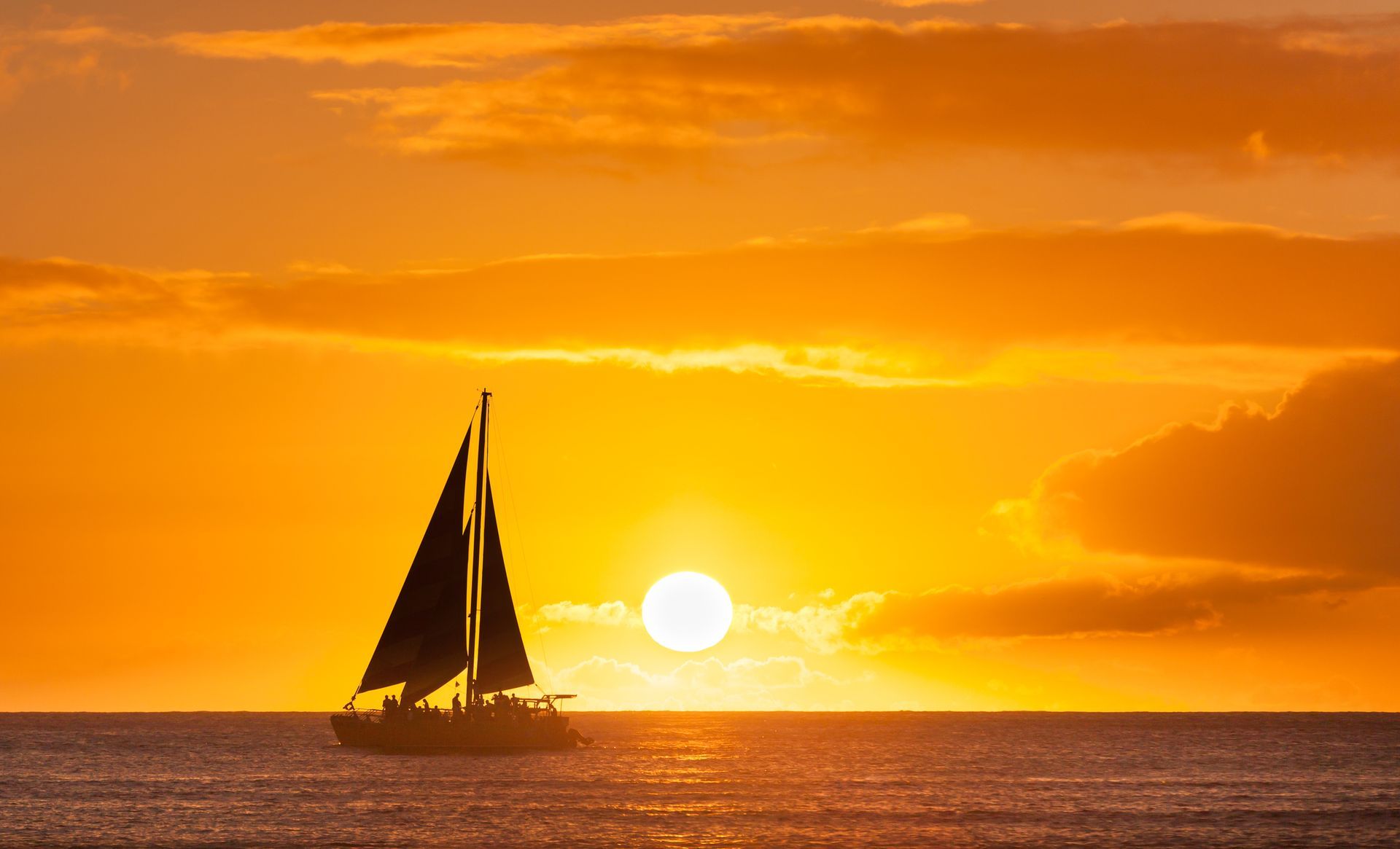 A sailboat is sailing in the ocean at sunset.