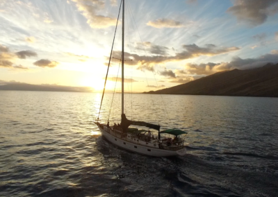 A sailboat is floating in the sea at sunset with hill on the background