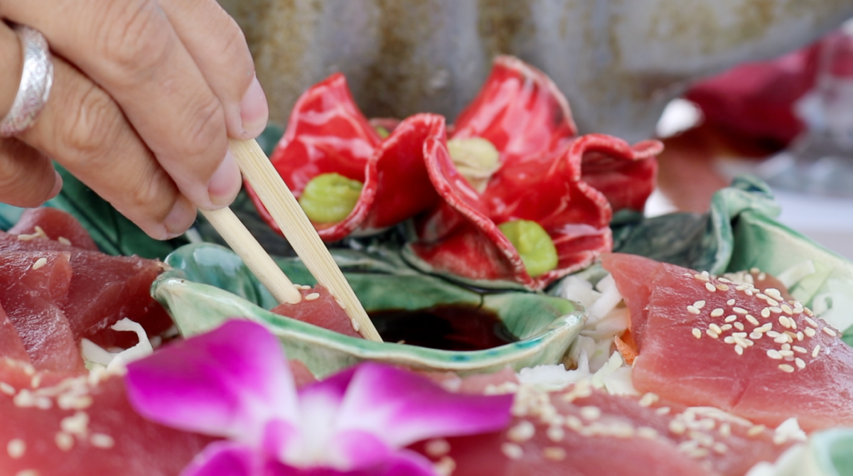 A person is dipping a flower in a bowl of food with chopsticks.