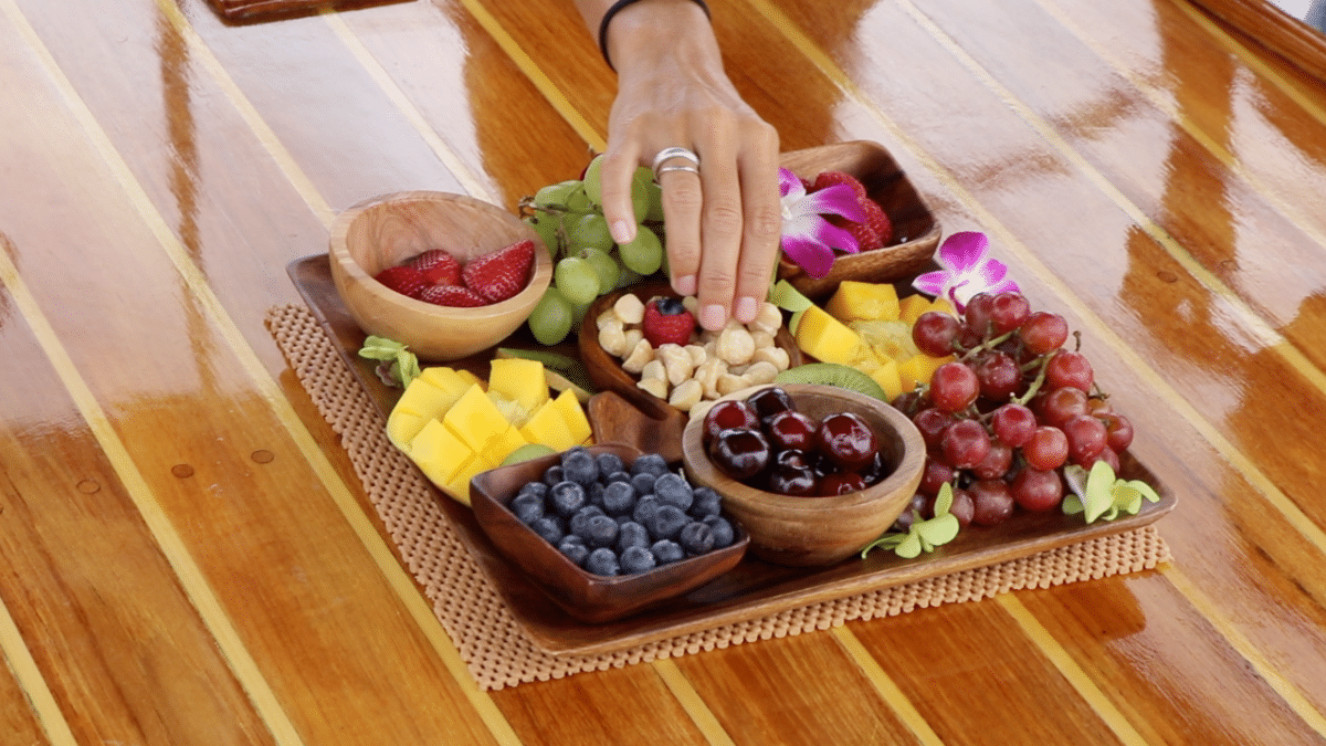 A person is putting fruit on a wooden tray on a wooden table.