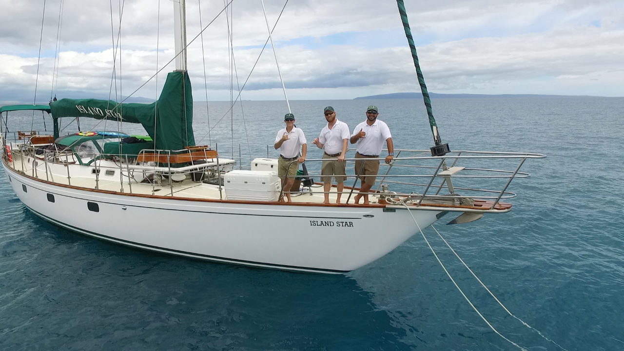 Three men are standing on the deck of a sailboat with the name tara on it
