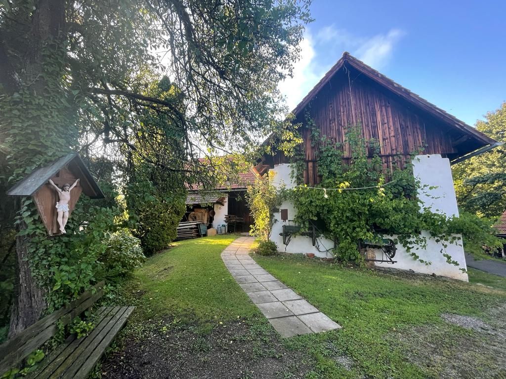 Der Pfad führt zu einem rustikalen Gebäude mit weinbewachsenen Wänden. Links steht ein Holzkreuz.