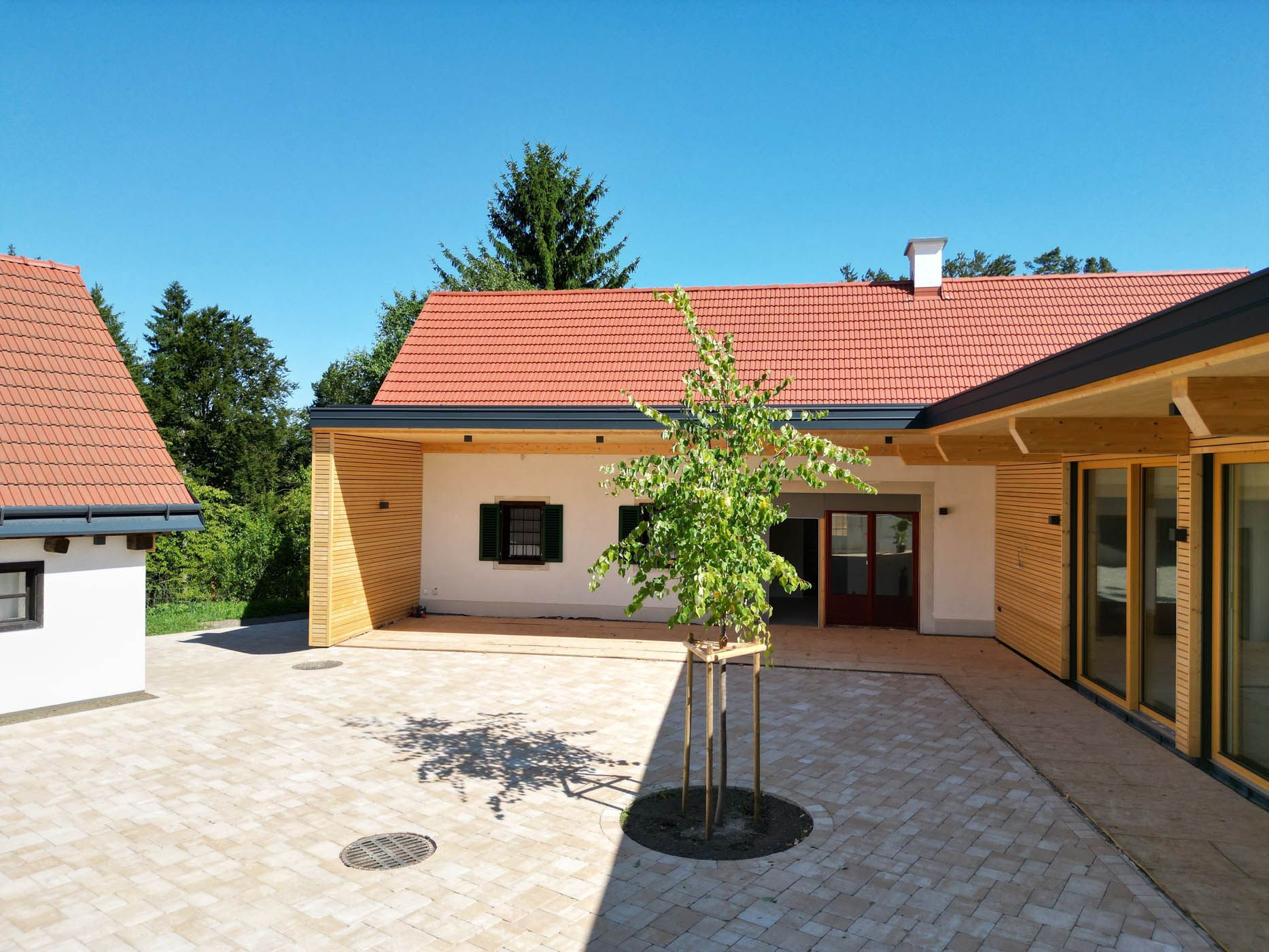 Innenhof von Gebäuden mit roten Ziegeldächern, hellen Wänden und Holzbalken an einem sonnigen Tag.