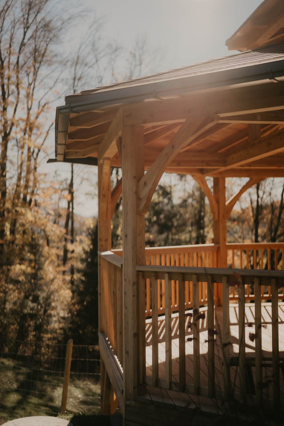 Holzterrasse und Pavillon, durch deren Bäume Sonnenlicht fällt.