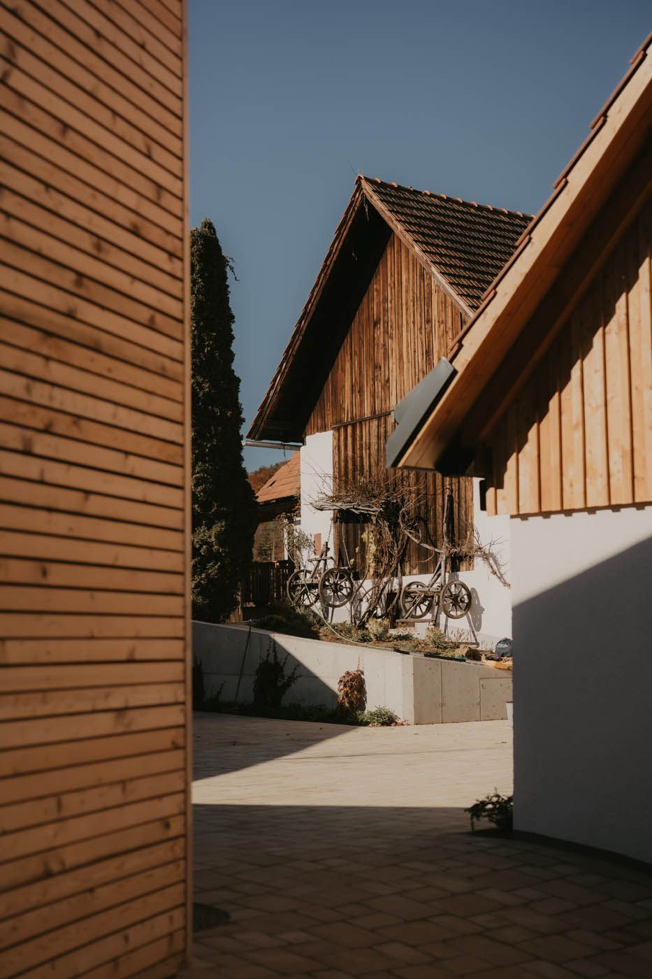 Holzbauten mit Ziegeldächern und einem gepflasterten Innenhof unter klarem, blauem Himmel.