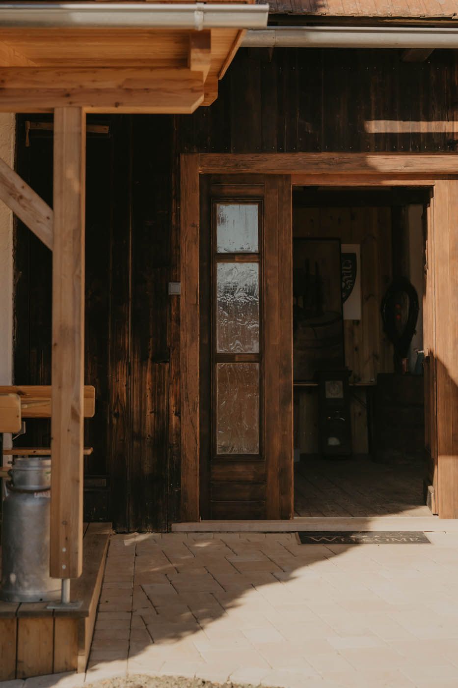 Holztür mit Glasscheibe, die in ein rustikales, sonnendurchflutetes Gebäude führt.