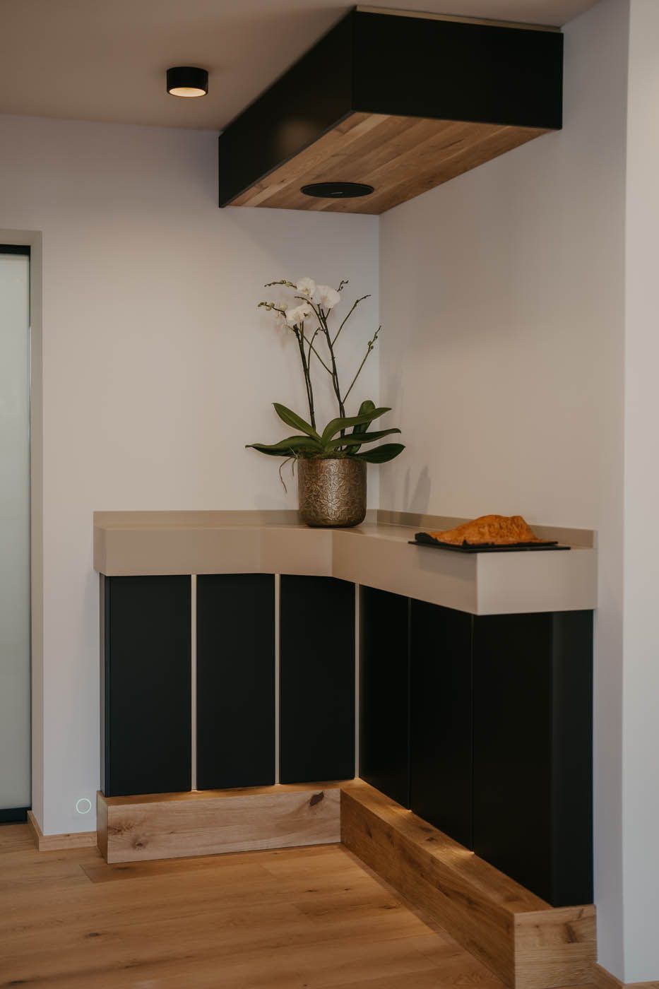 Küchentheke in Ecke, mit schwarzen Schränken, Holzelementen und einer Orchidee.