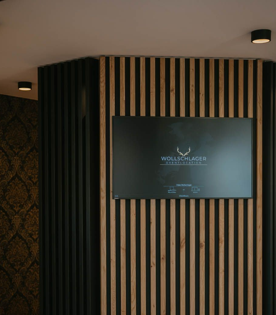 Fernsehbildschirm an einer Holzlattenwand, auf dem ein Logo zu sehen ist. Innenansicht eines Zimmers.