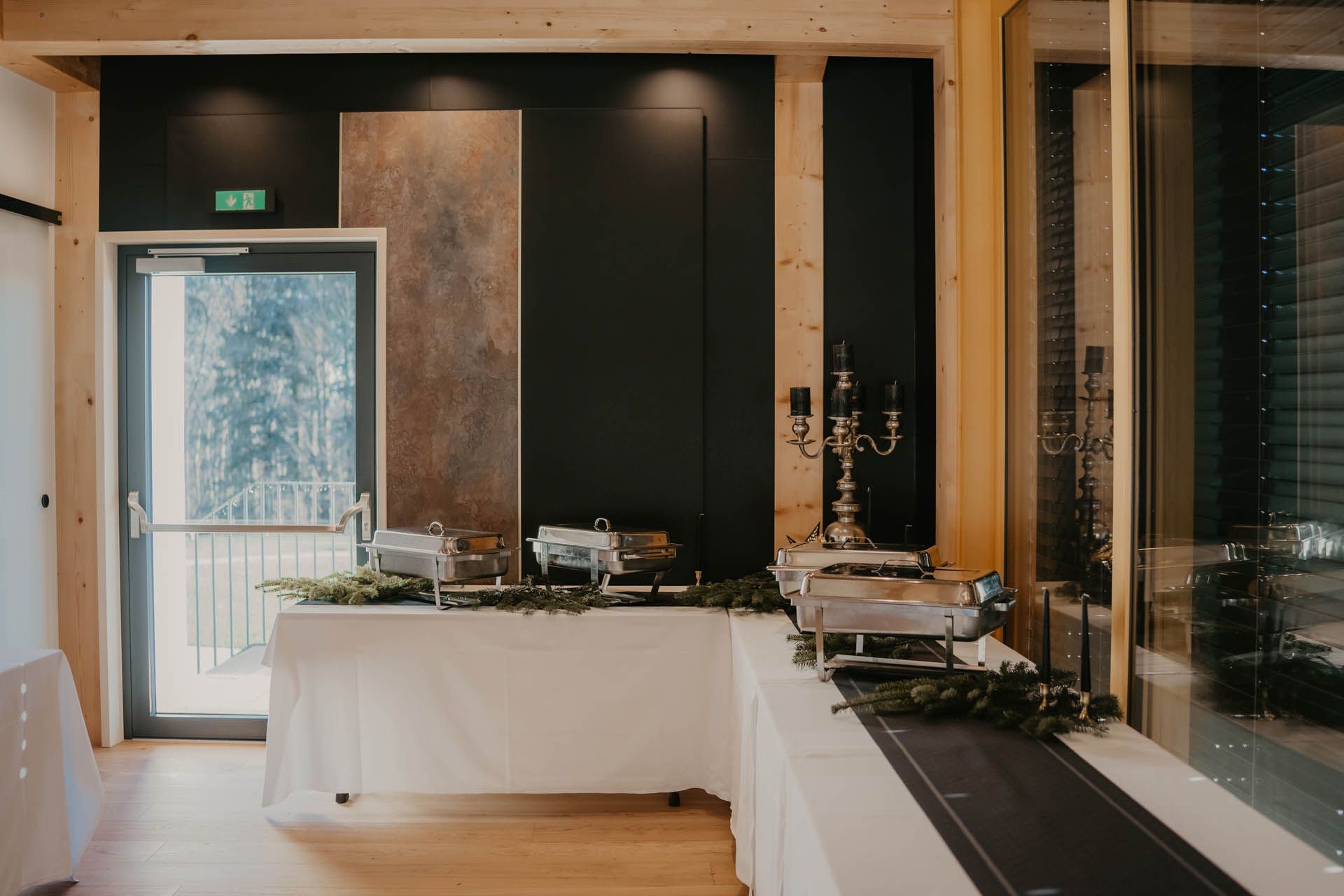 Buffettisch mit Speisenwärmern, mit weißer Tischwäsche bedeckt, vor einer dunklen Akzentwand.