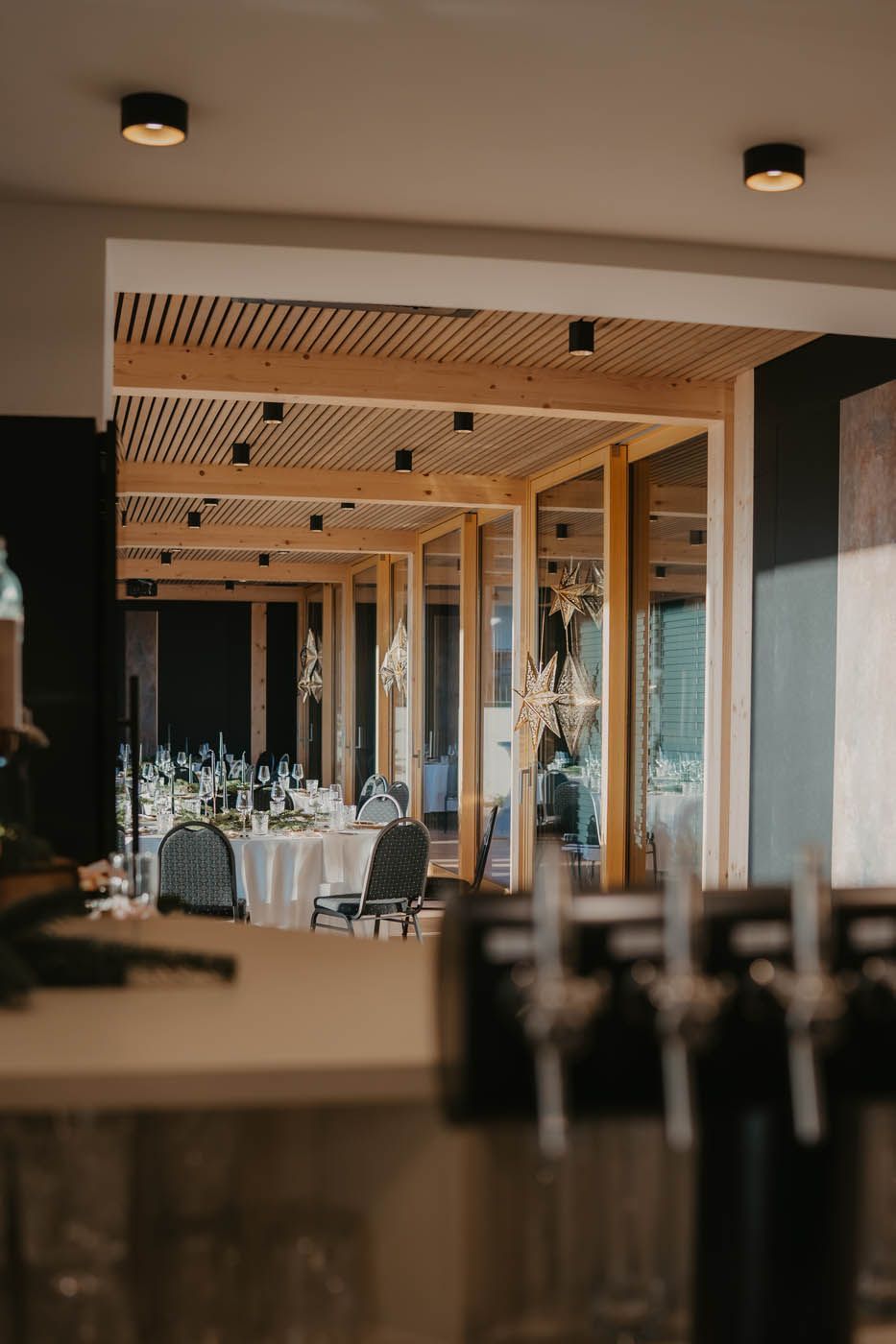 Restaurantinterieur mit gedeckten Tischen, Blick durch eine offene Tür. Holzbalken und Einbauleuchten.