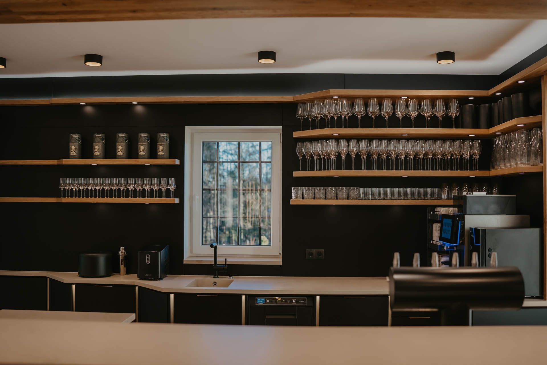 Bar-Interieur mit schwarzen Wänden, Holzregalen mit Gläsern und einer weißen Theke.