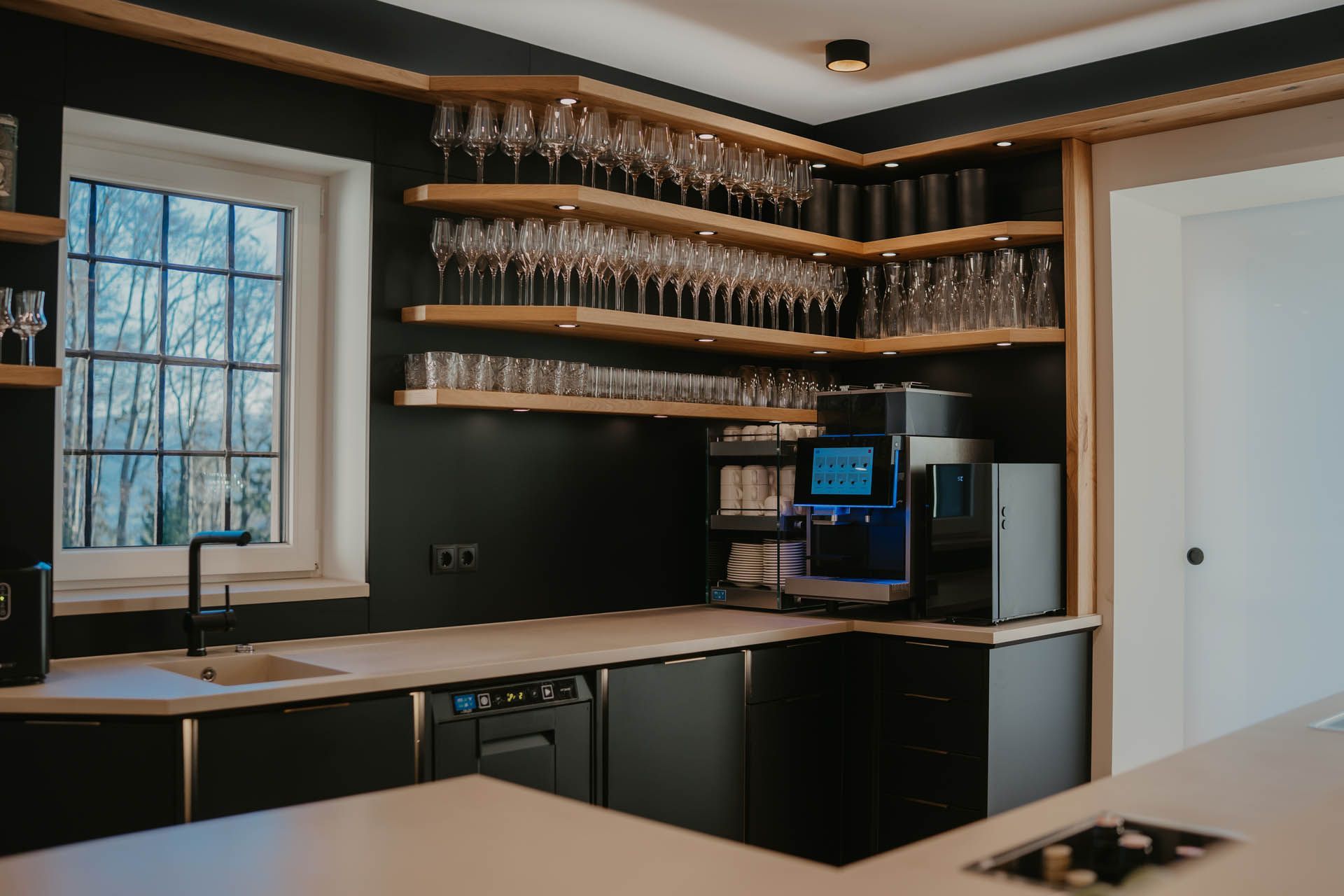 Eckbarbereich mit Weingläsern, Espressomaschine und schwarzen Schränken.