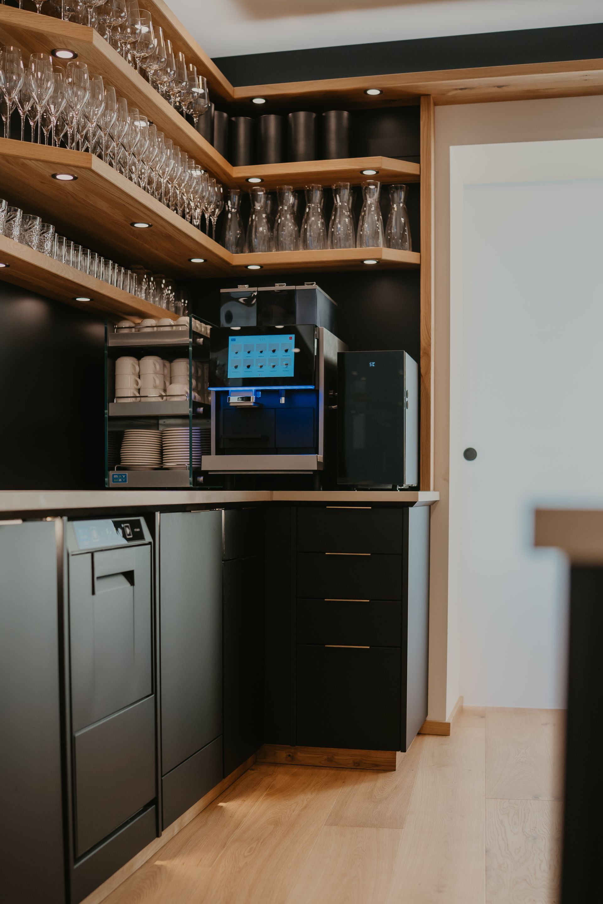 Eckbar mit Regalen für Gläser, eingebauter Espressomaschine, schwarzen Schränken und Geschirrspüler.