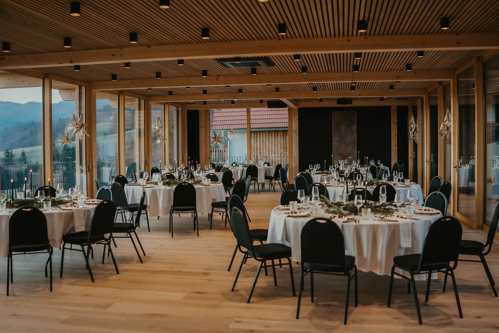 Hochzeitsempfangssaal mit runden Tischen, schwarzen Stühlen und Panoramafenstern.