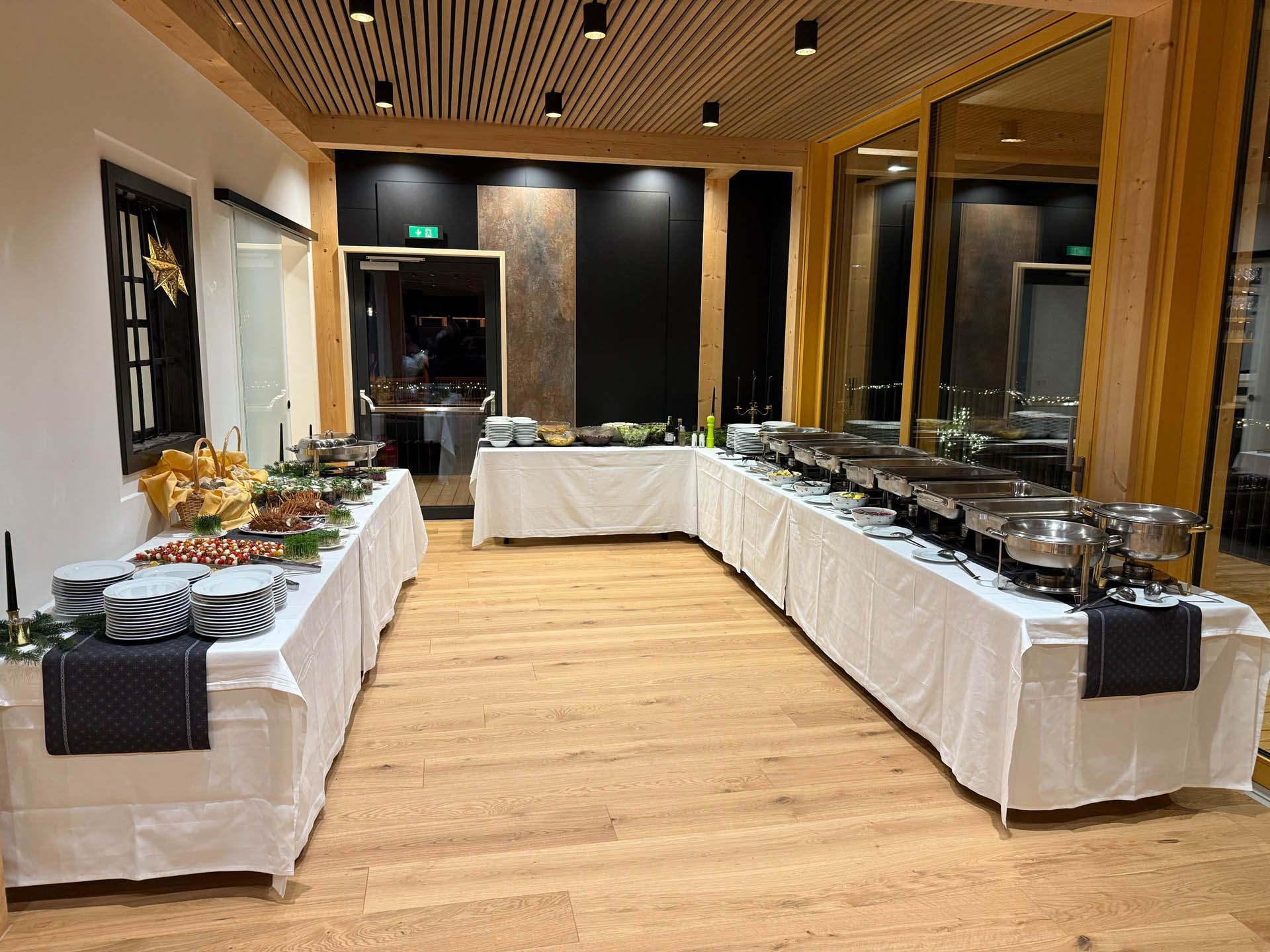 Buffetaufbau in einem holzgetäfelten Raum mit abgedeckten Tischen, auf denen Speisen präsentiert werden, und Warmhaltebehältern.