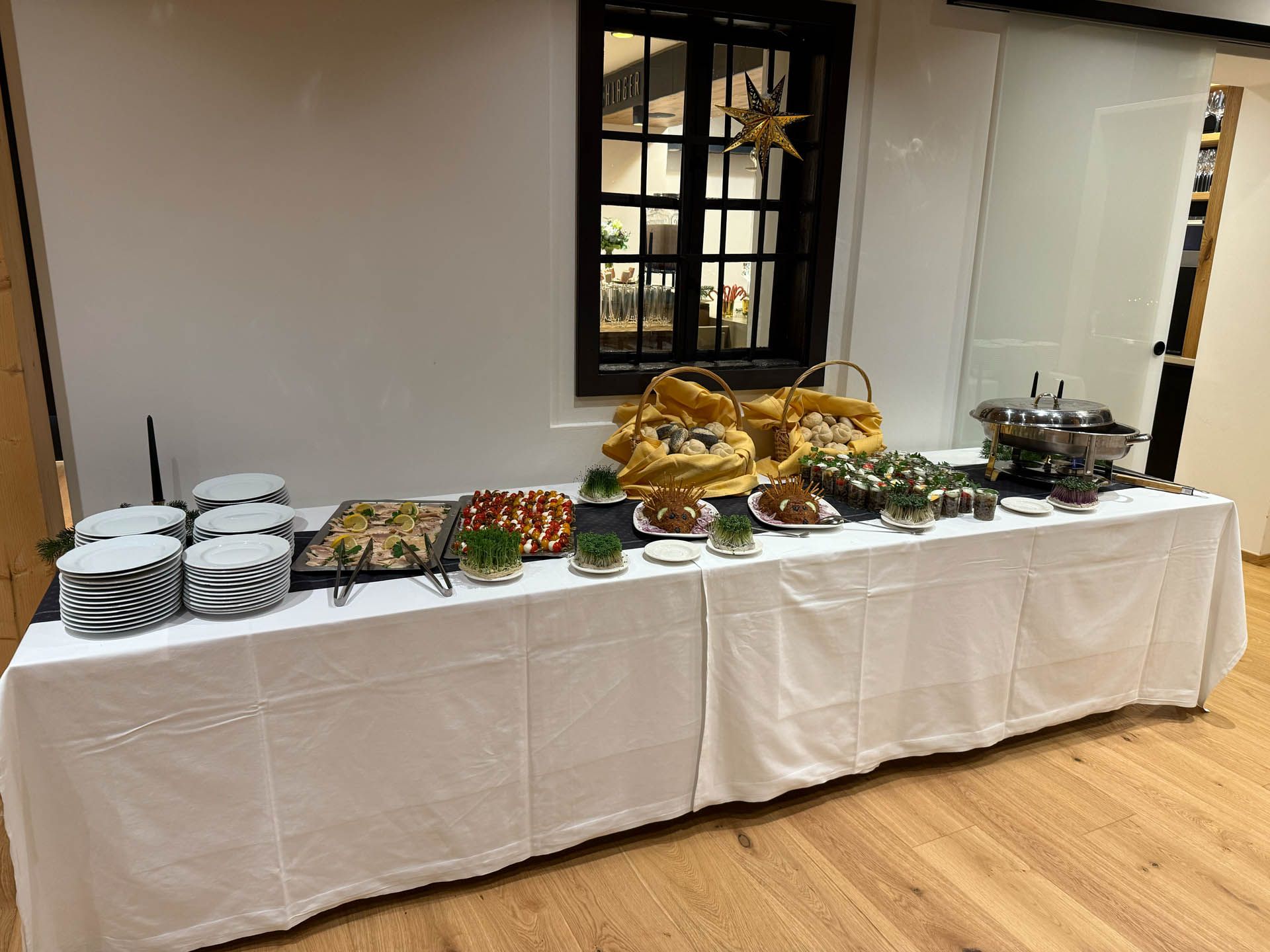 Buffet mit verschiedenen Speisen, weißer Tischdecke und Holzboden. Über dem Tisch befindet sich ein Fenster mit Sternenverzierung.