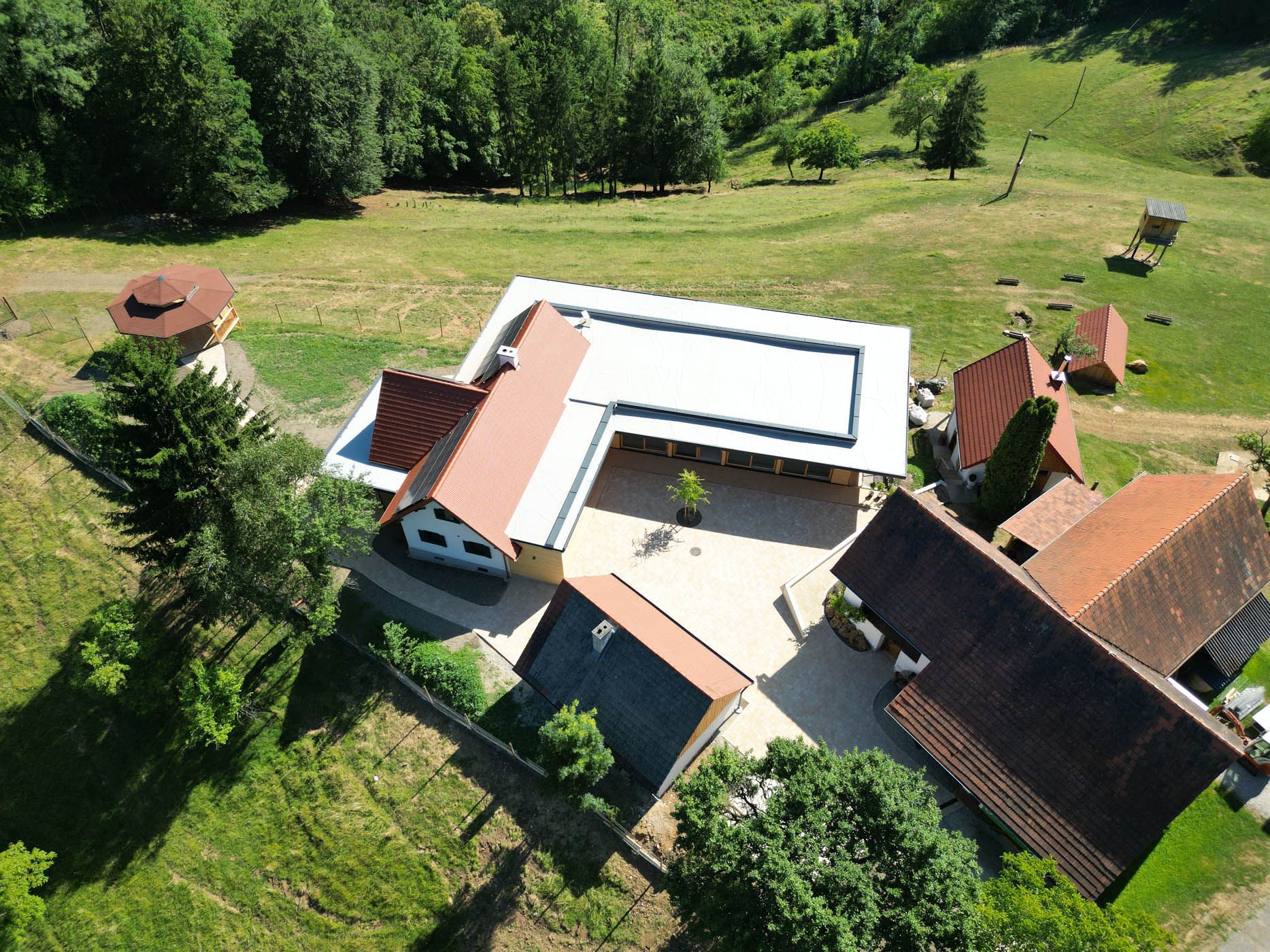 Luftaufnahme eines Gebäudekomplexes mit roten Ziegeldächern, umgeben von grünem Gras und Bäumen.