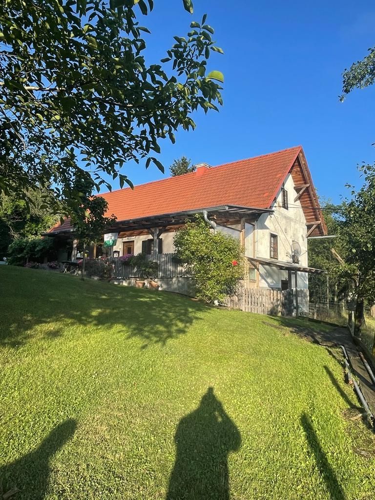Steinhaus mit rotem Ziegeldach auf einem grasbewachsenen Hügel unter klarem, blauem Himmel.