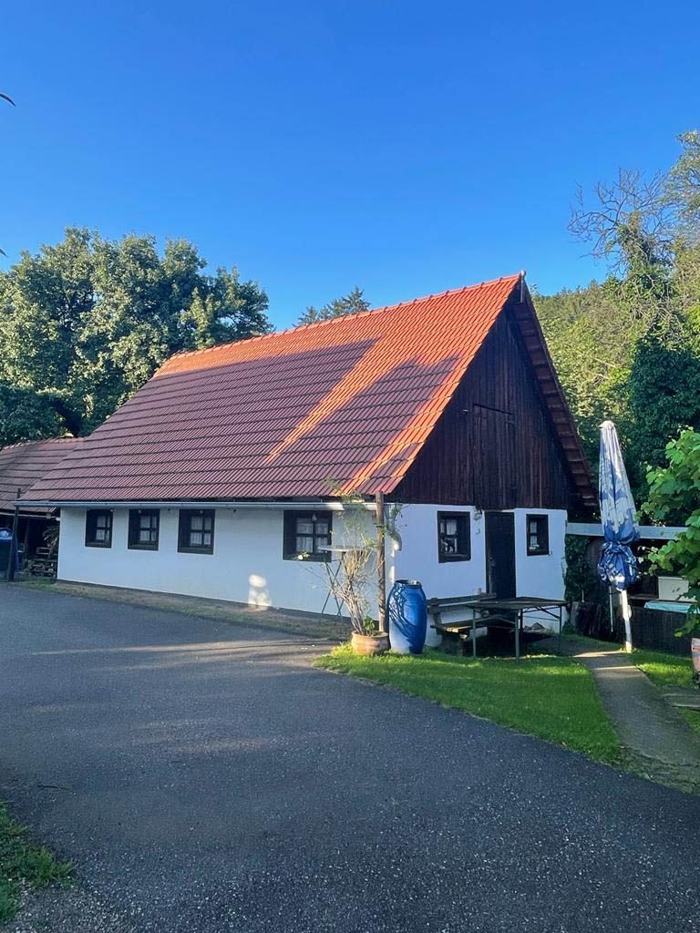 Weißes Gebäude mit rotem Ziegeldach, gelegen an einer von Bäumen gesäumten Straße unter klarem, blauem Himmel.