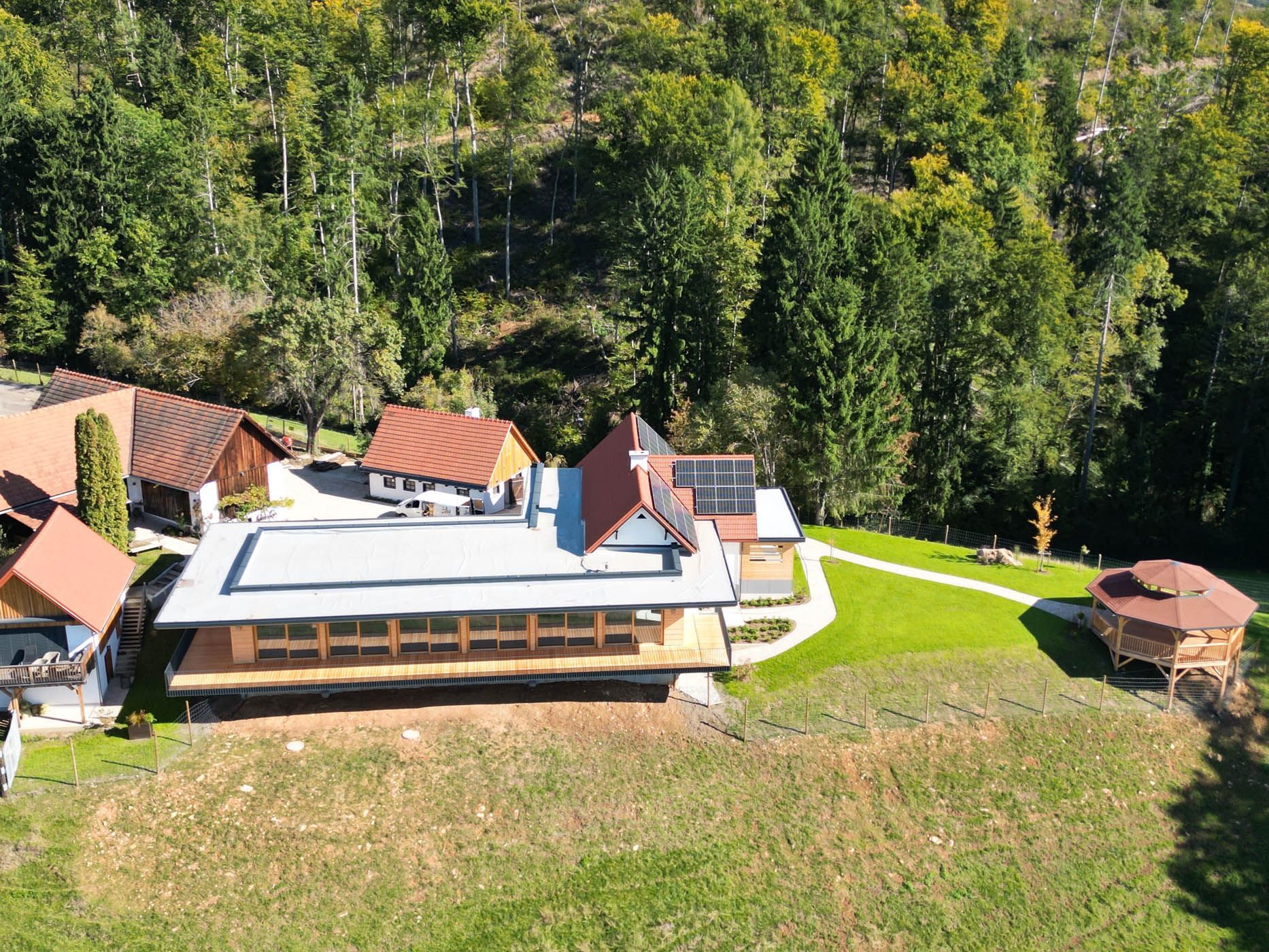 Luftaufnahme eines Gebäudes mit rotem Dach, umgeben von grünem Gras und Bäumen.