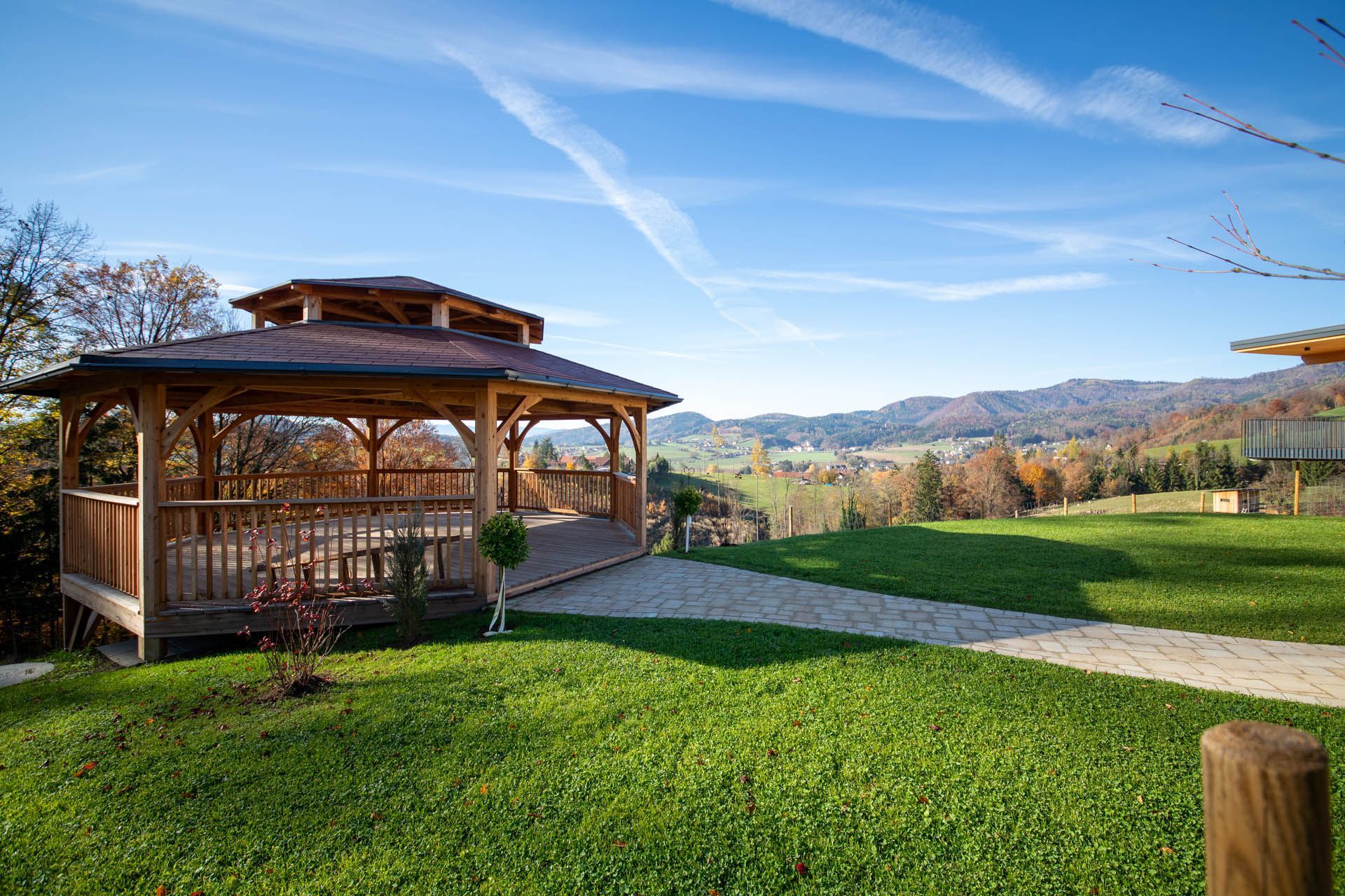 Ein hölzerner Pavillon mit Blick auf ein grünes Feld und ferne Hügel unter blauem Himmel.