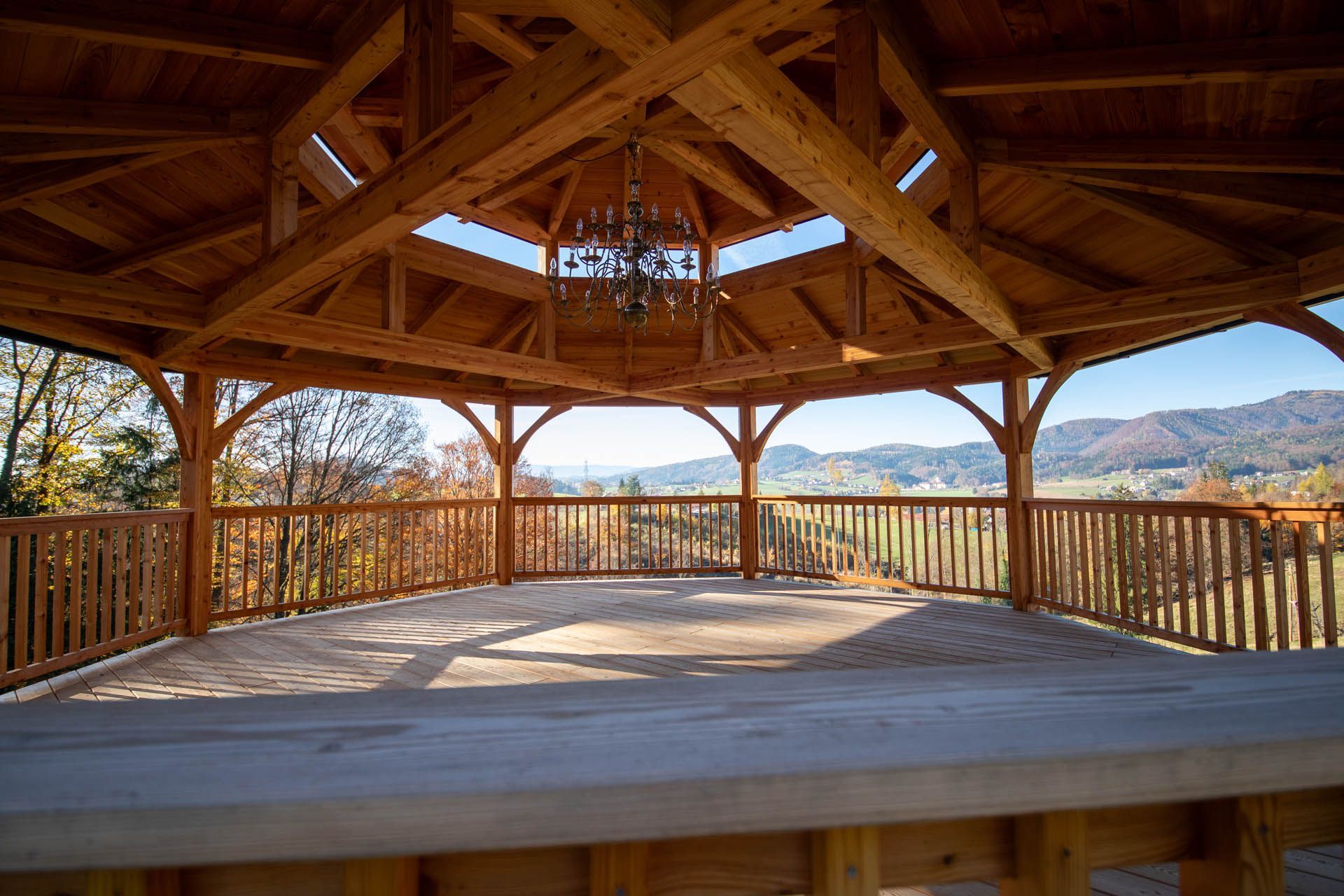 Holzpavillon mit Bergblick, braunem Geländer und Kronleuchter im Inneren.