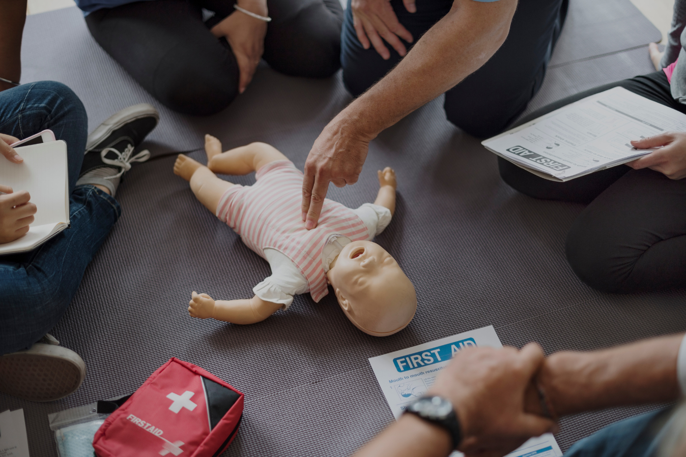 A group of people are sitting around a dummy of a baby.