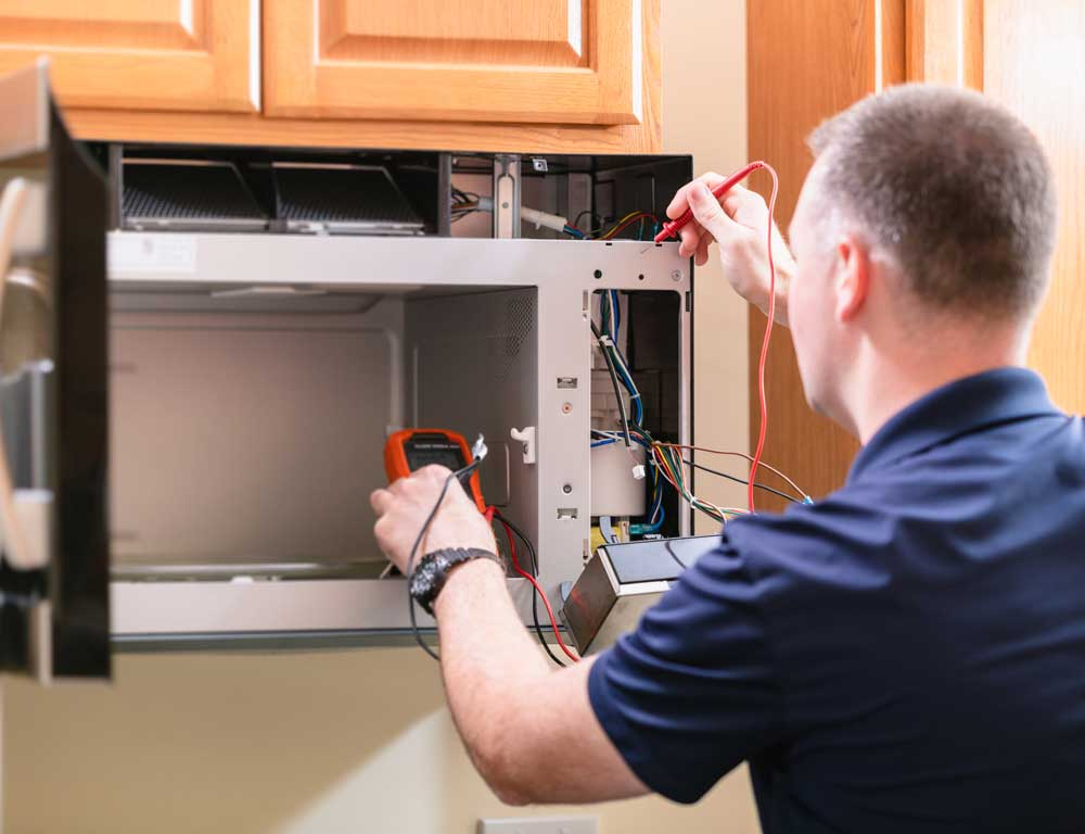 a man is fixing a microwave with a multimeter .
