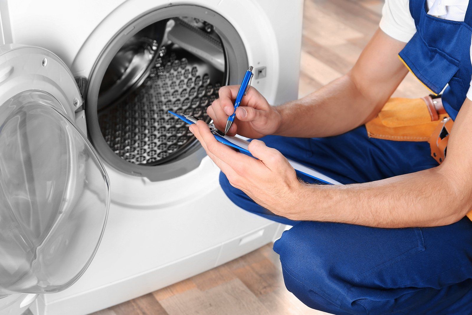 a man is kneeling down in front of a washing machine and writing on a clipboard .