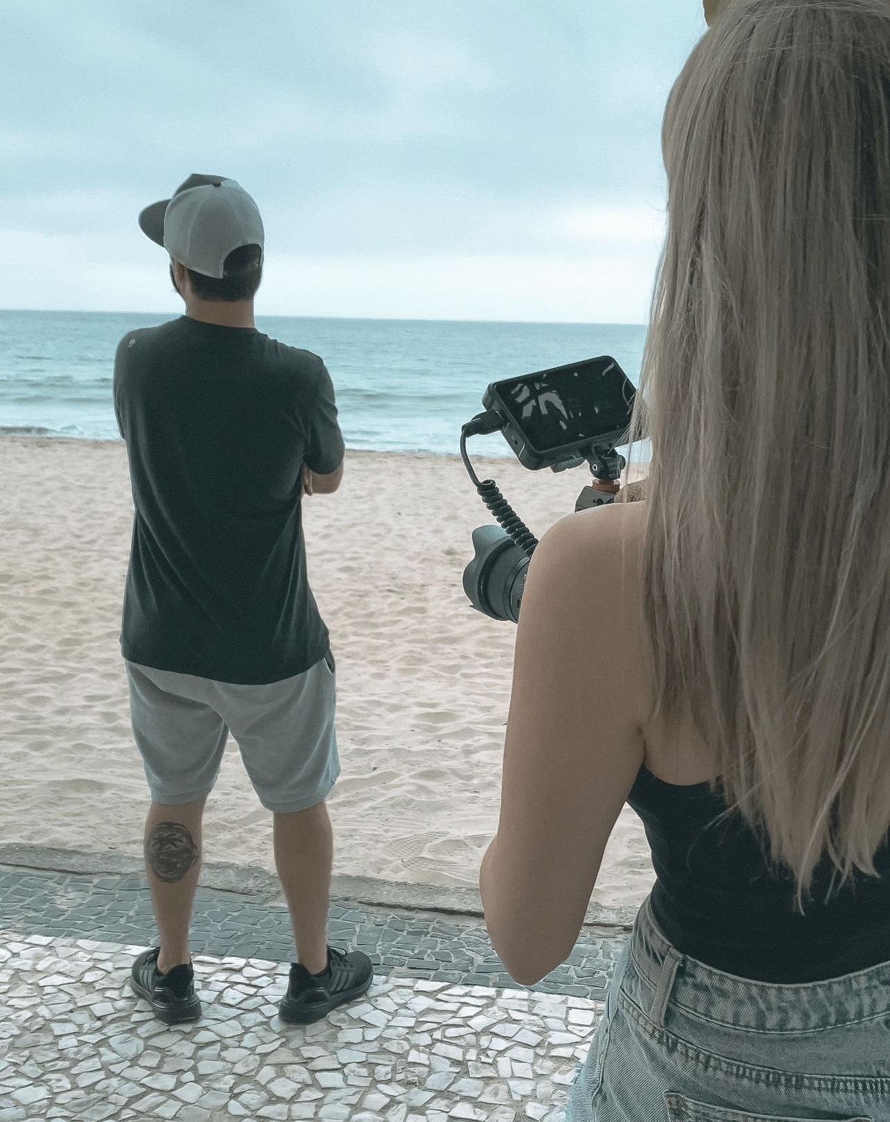 a woman is holding a camera while a man stands on the beach .