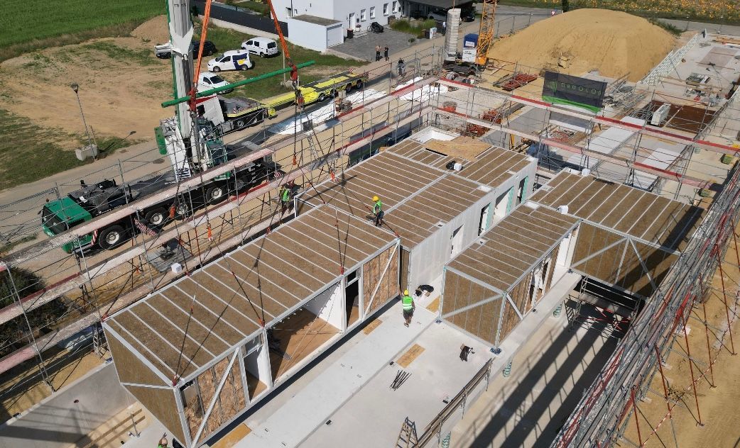 Baustelle für modulares Bauen: Kran hebt vorgefertigte Einheiten auf ein Fundament.