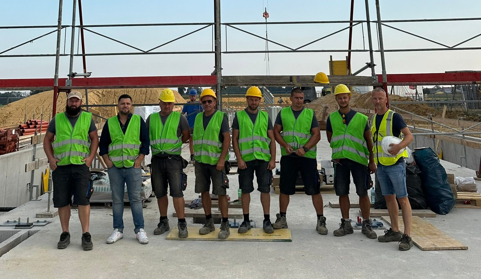 Eine Gruppe von Bauarbeitern in Westen und Schutzhelmen posiert auf einer Betonfläche mit Gerüst.