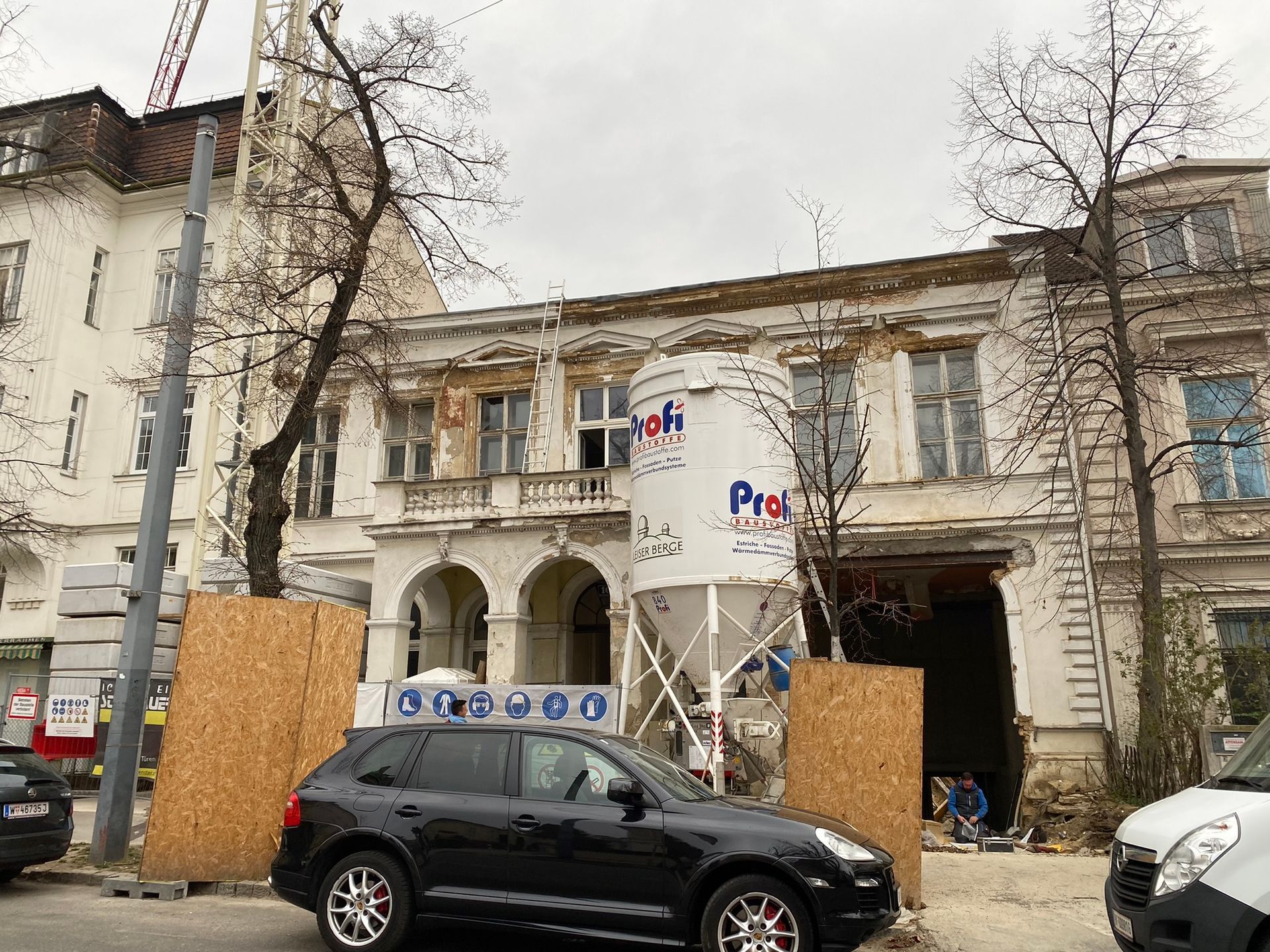 Gebäude im Bau, großer weißer Container, schwarzes Auto auf der Straße geparkt, grauer, bewölkter Himmel.