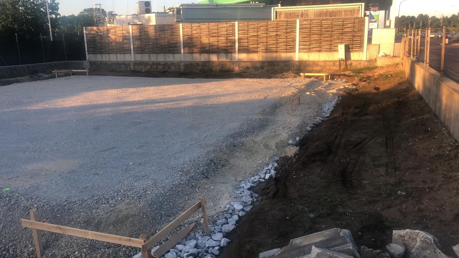 Mit Kies bedeckte Baustelle mit Stützmauer, Zaun und Erde; tagsüber.