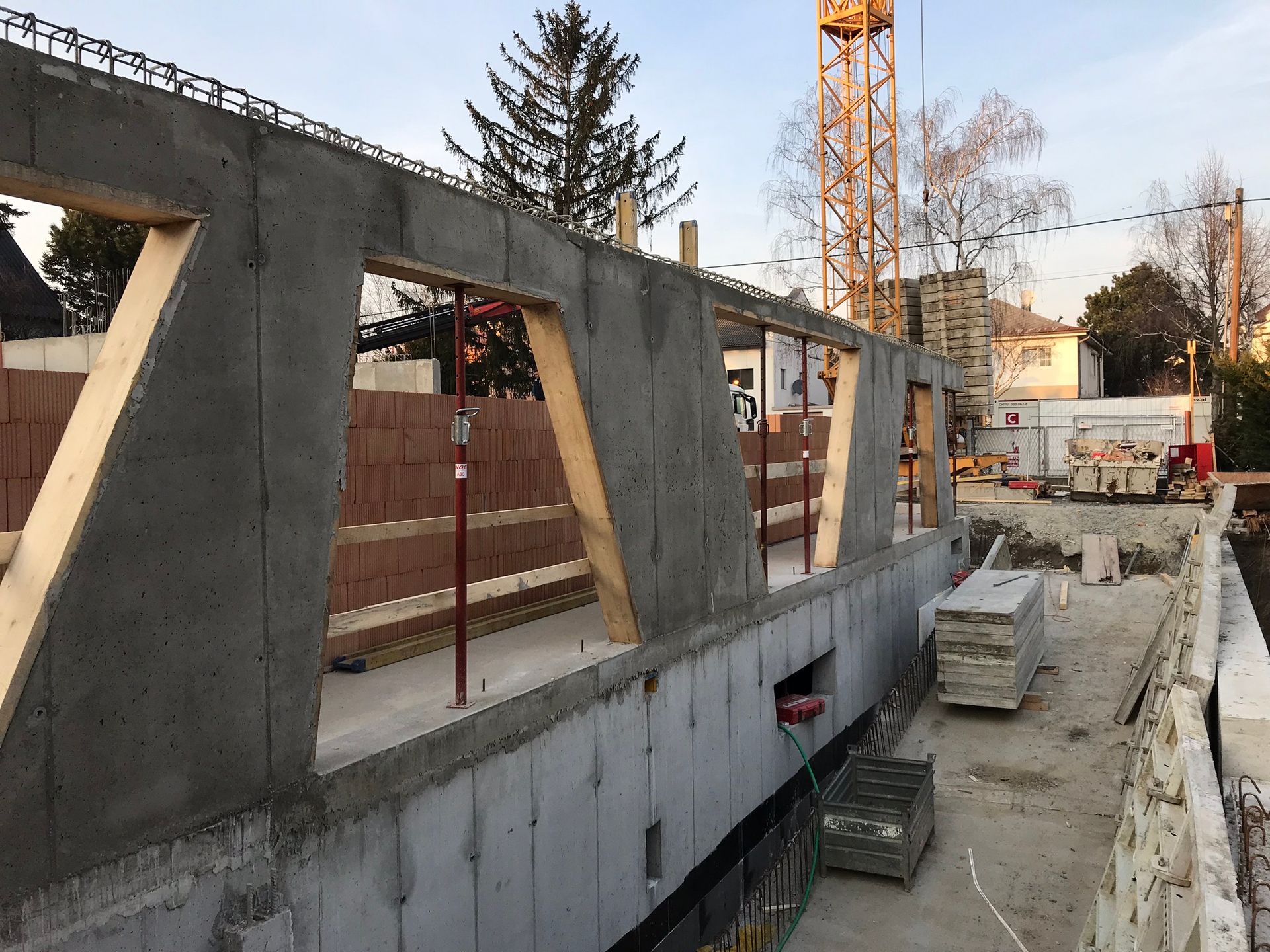 Baustelle mit Betonwänden, Holzstützen und einem Kran.