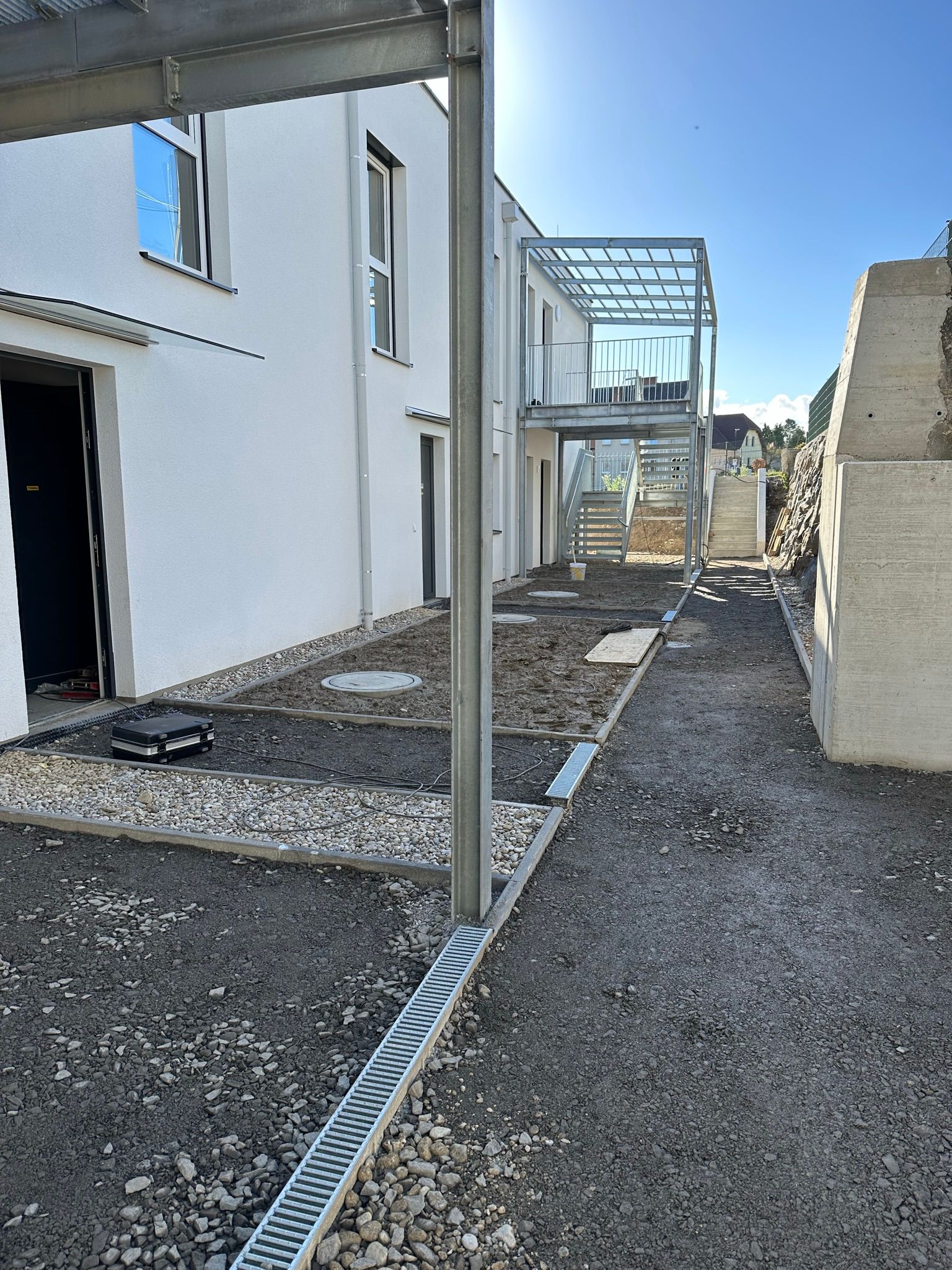 Baustelle mit Schotterweg, Metalltreppe und weißem Gebäude.
