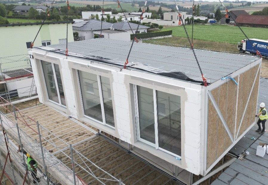 Eine modulare Baueinheit wird mit einem Kran auf eine Baustelle herabgelassen. 