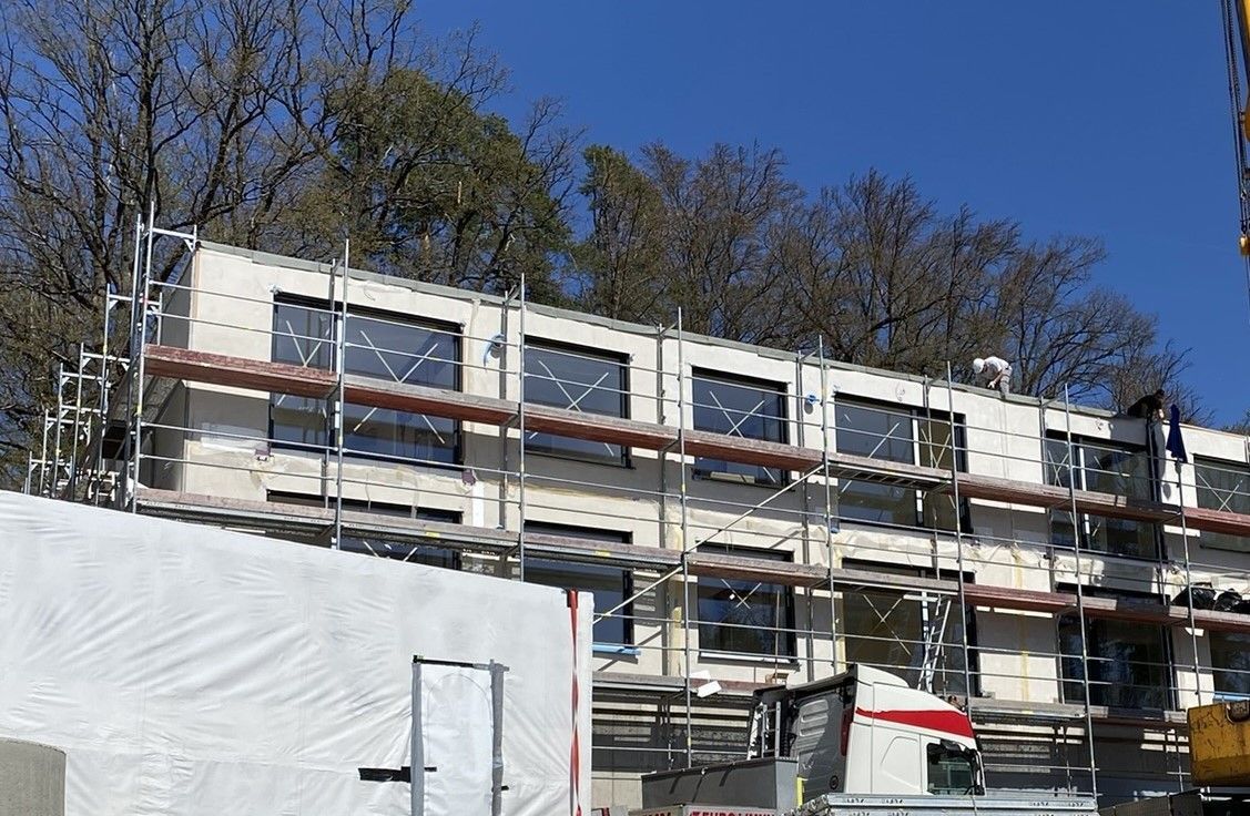Gebäude im Bau mit Gerüst. Außenansicht eines hellen Gebäudes mit mehreren Fenstern und Bäumen im Hintergrund.
