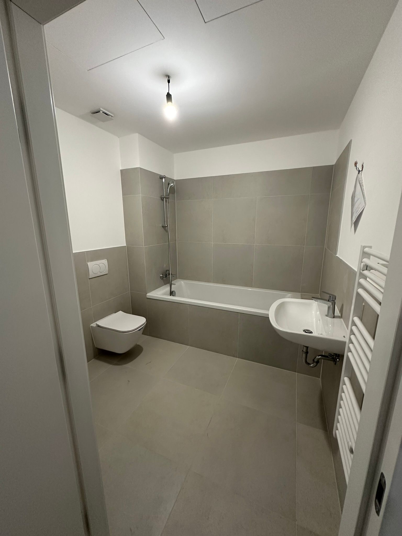 Badezimmer mit grauen Fliesen und weißen Armaturen, einschließlich Toilette, Waschbecken und Badewanne.