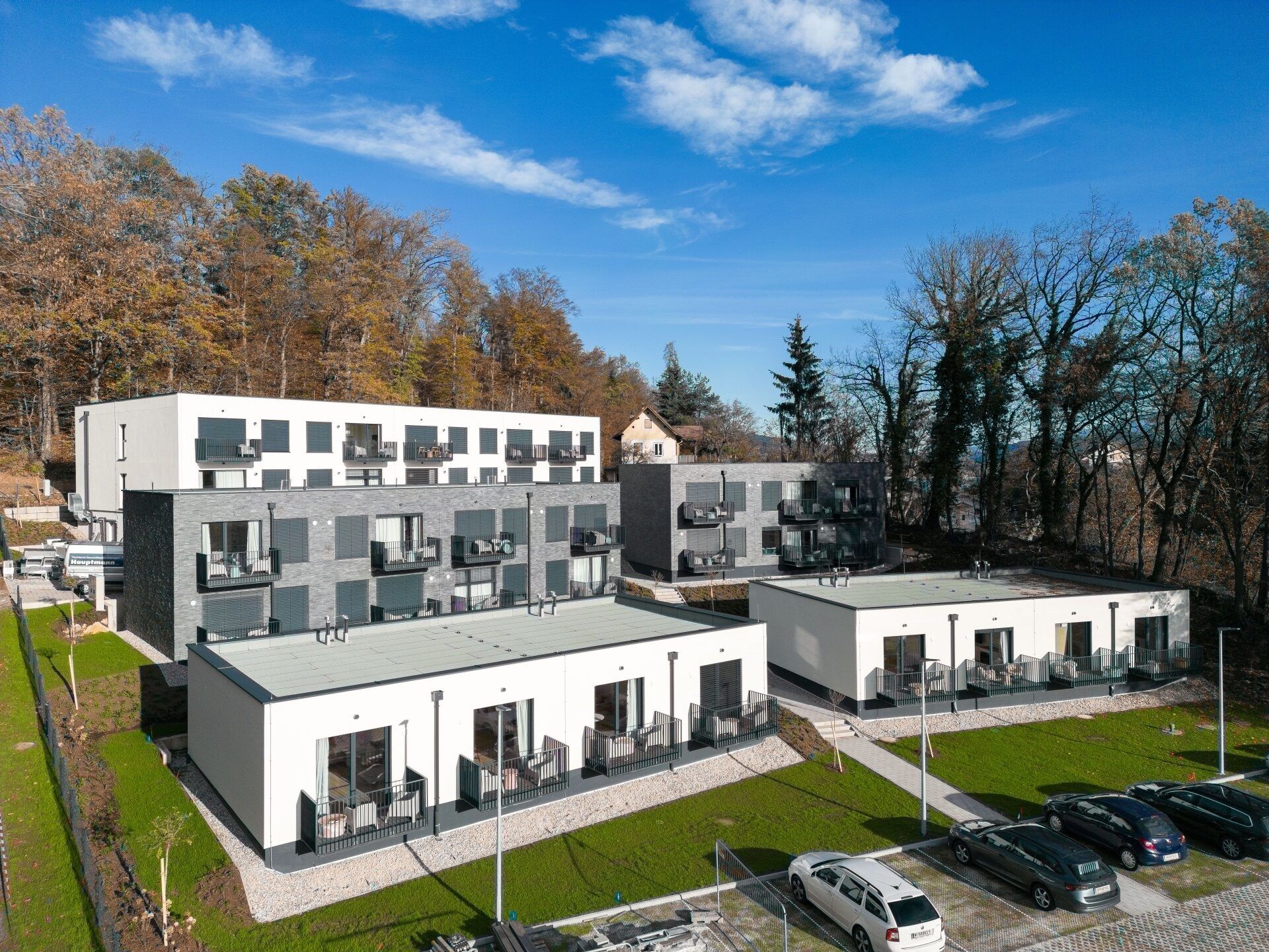 Moderne Apartmentgebäude mit Balkonen und Parkplätzen, umgeben von einem Wald.
