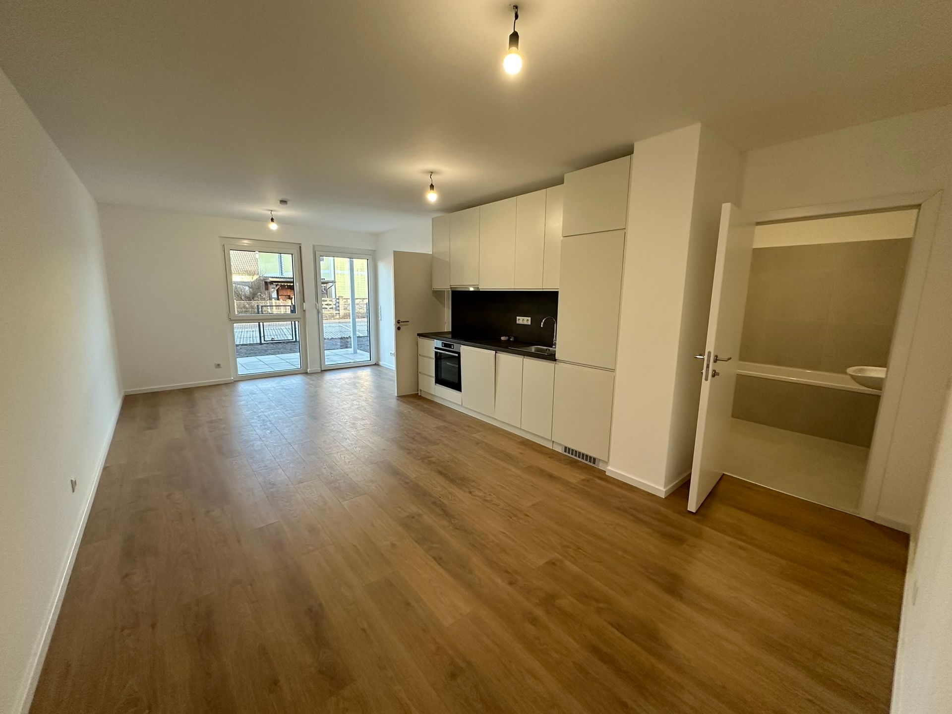 Heller Wohnraum mit Hartholzböden, weißen Küchenschränken und einer Tür zu einem Außenbereich.