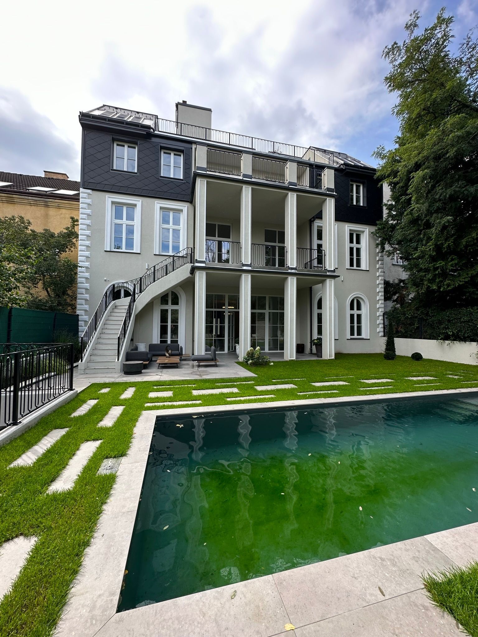 Zweistöckiges modernes Haus mit Pool, Rasen und Wendeltreppe. Grau-weiße Fassade. Grünes Poolwasser.