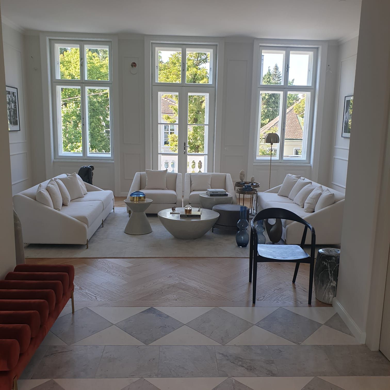 Elegantes Wohnzimmer mit cremefarbenen Sofas, großen Fenstern mit Blick auf Bäume und Marmorböden.