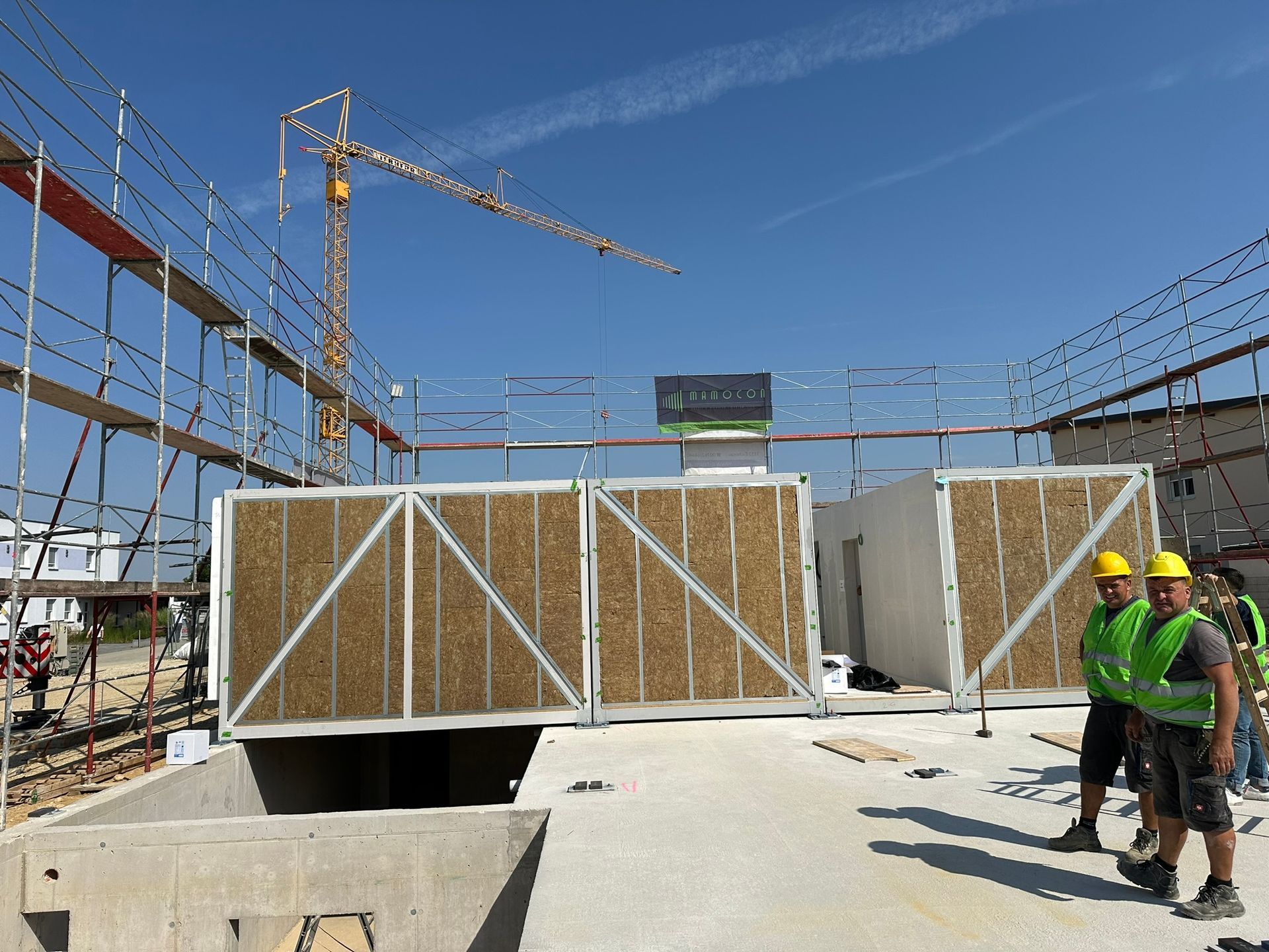 Baustelle mit zwei Arbeitern in Westen, einem Kran und vorgefertigten Bauplatten.