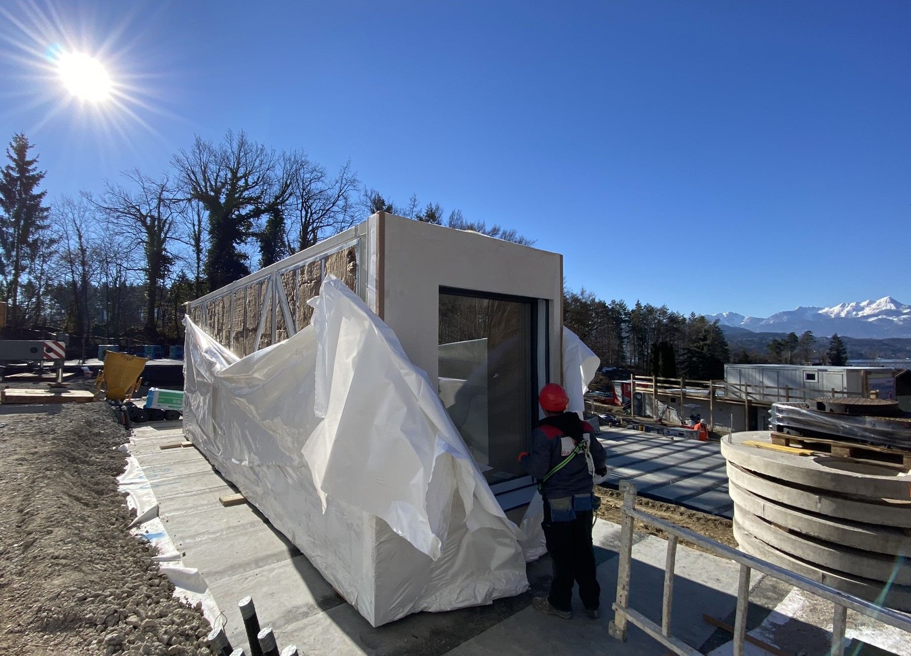 Baustelle: Eine Person mit einem roten Hut steht vor einem kleinen, modernen Gebäude,