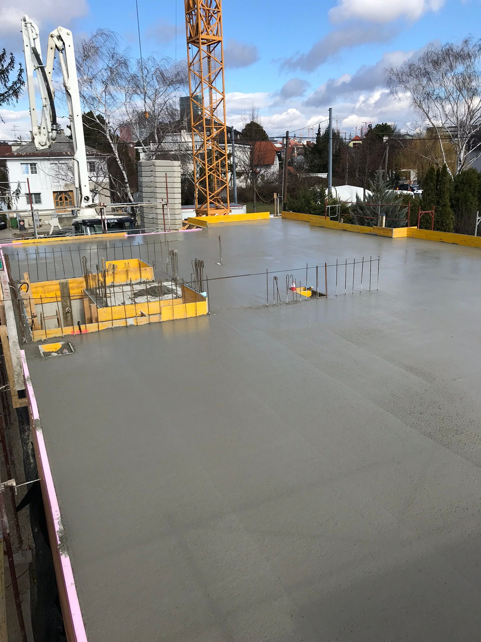 Baustelle mit frisch gegossenem Beton; Kran und Gebäude im Hintergrund.