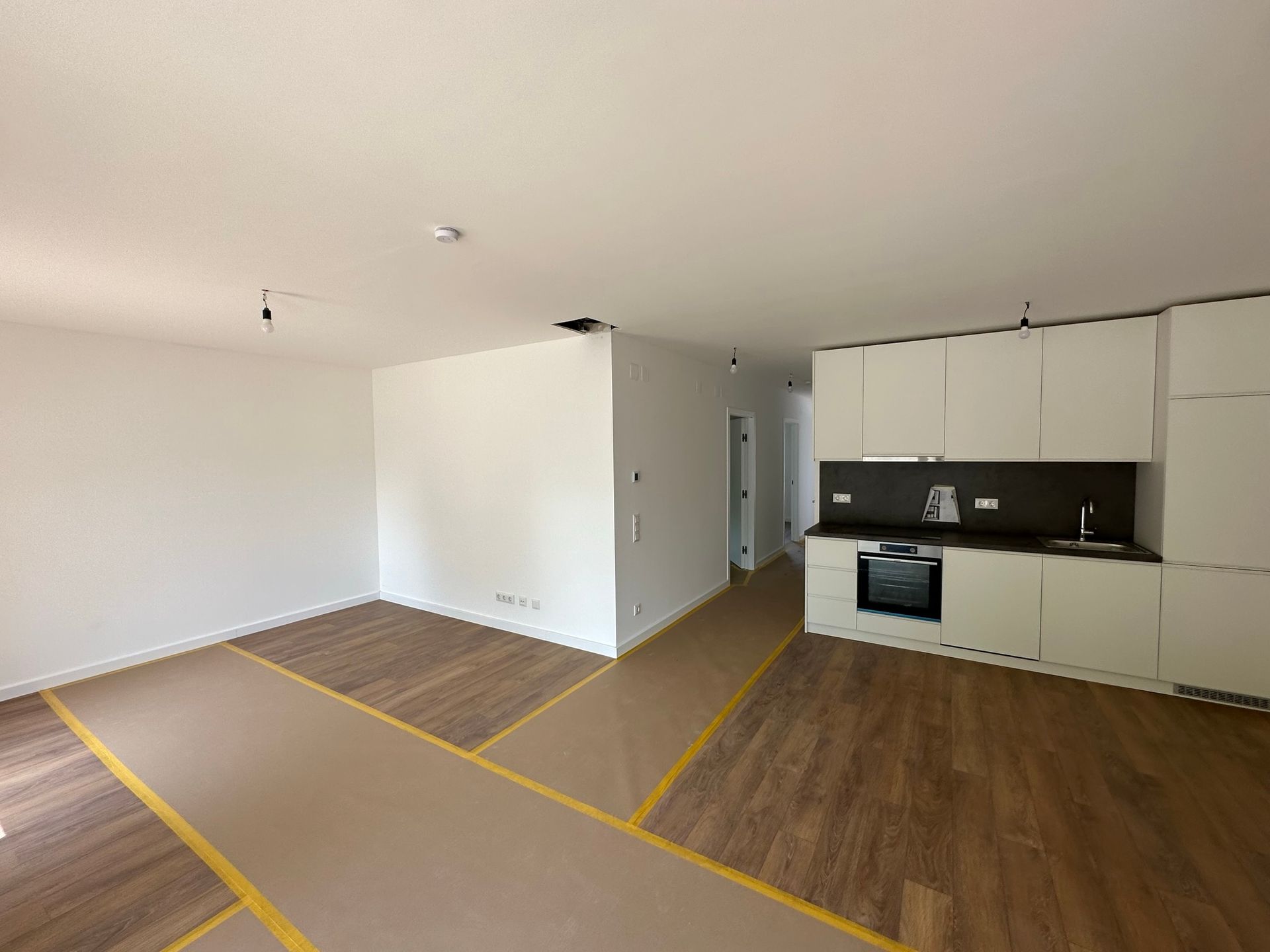 Leere Wohnung mit Hartholzböden, weißen Wänden und einer kleinen Küche.