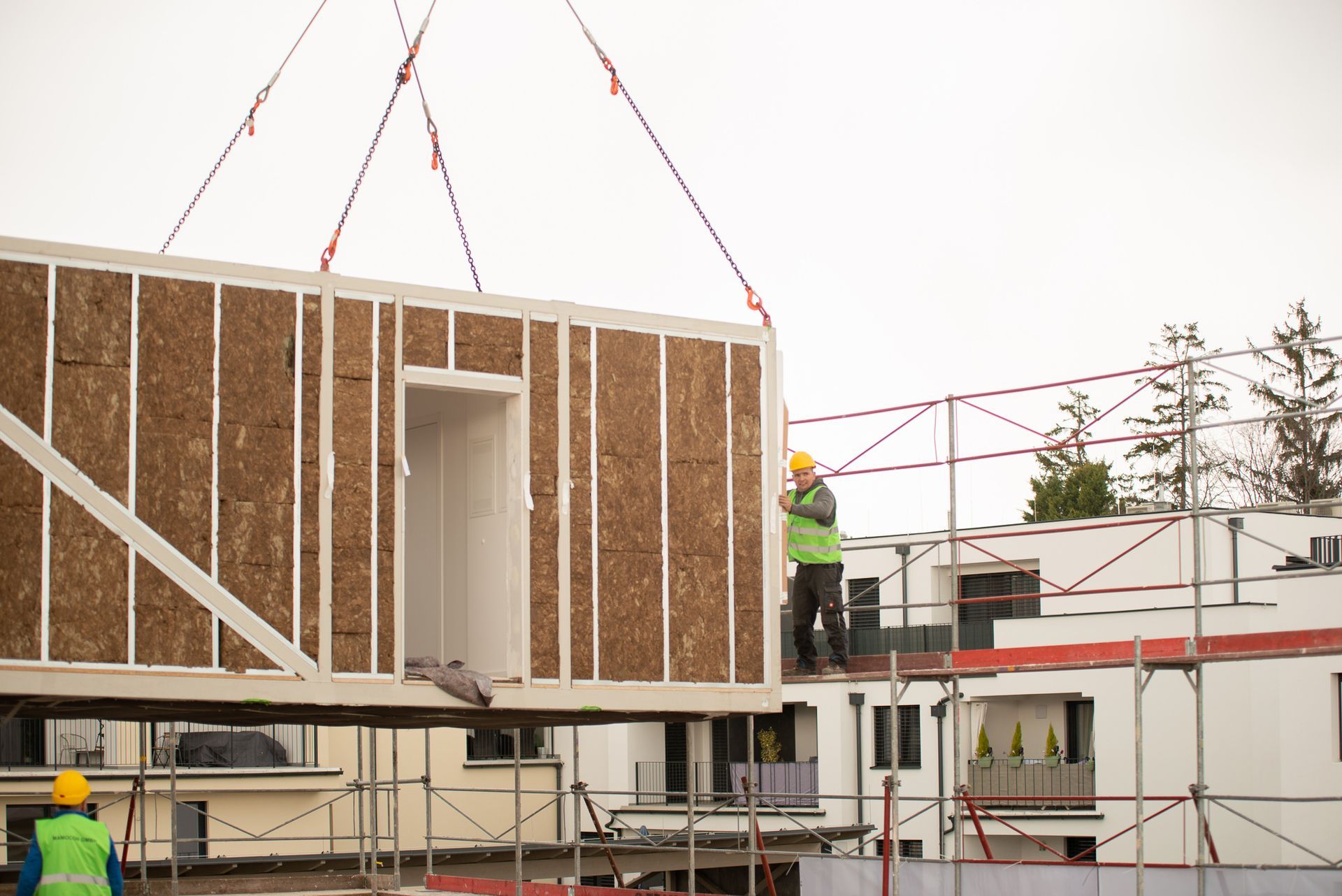 Bauarbeiter heben auf einer Baustelle ein modulares Bauelement mit einem Kran an.