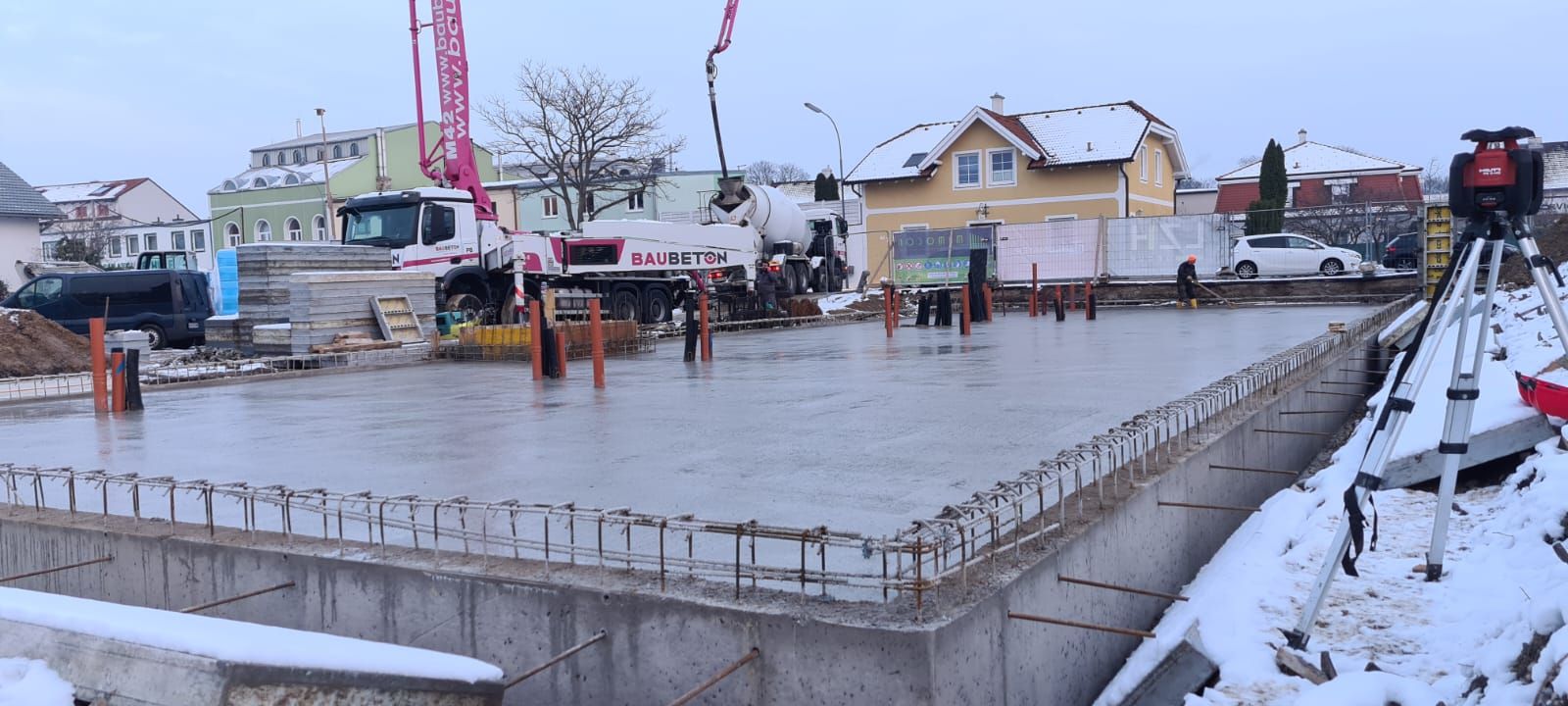 Baustelle, auf der nasser Beton in eine rechteckige Form gegossen wird; Schnee auf dem Boden.