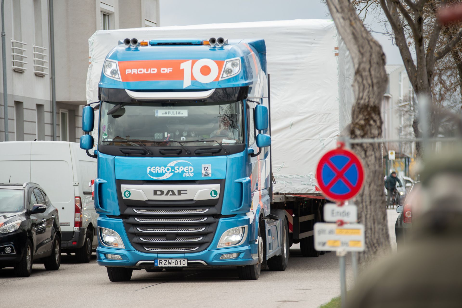 Blauer DAF-Sattelzug mit weißem Anhänger auf einer Straße. Schild weist auf Parkverbot hin.